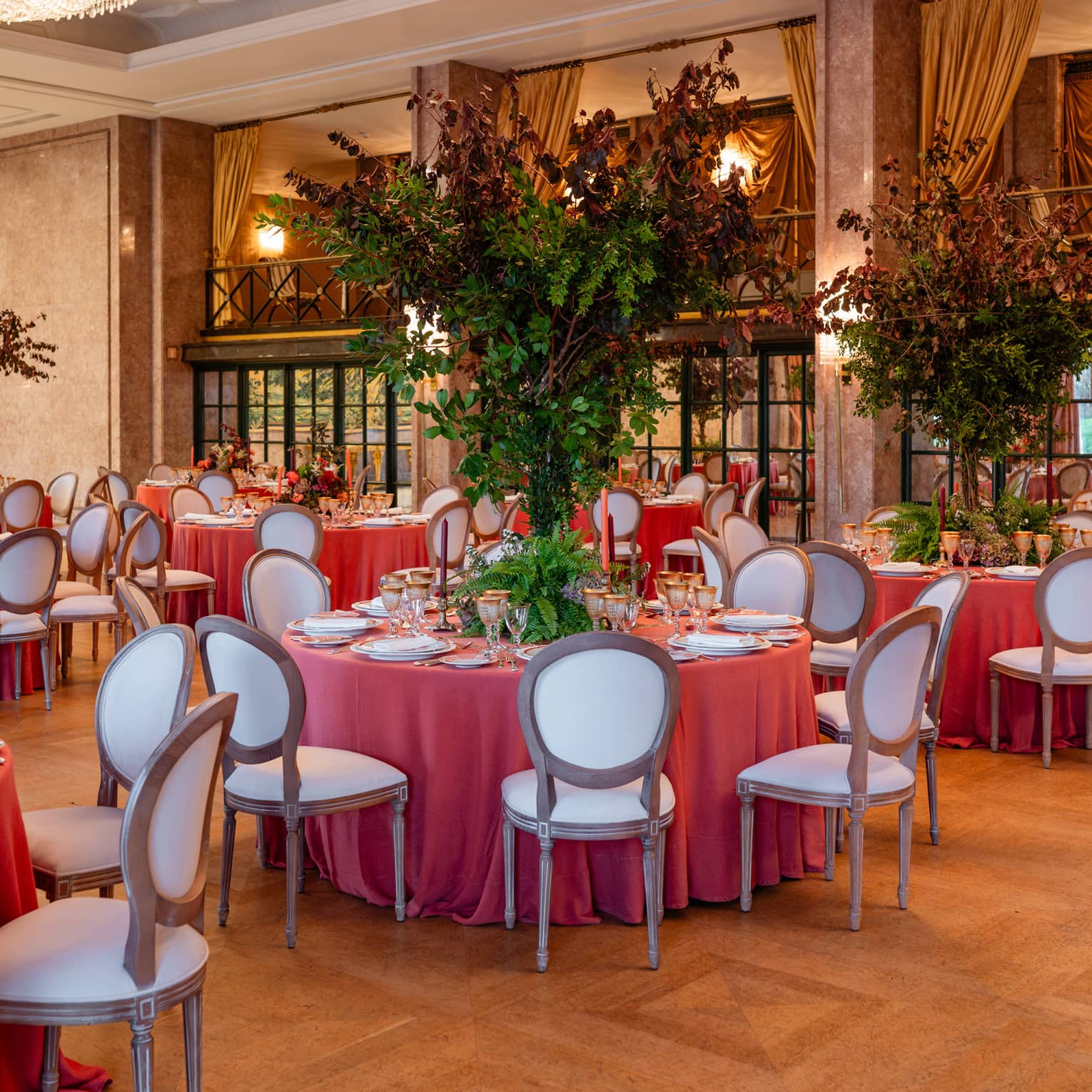 Elegant ballroom set for a formal event, with table rounds featuring coral-coloured tablecloths and tall floral centrepieces