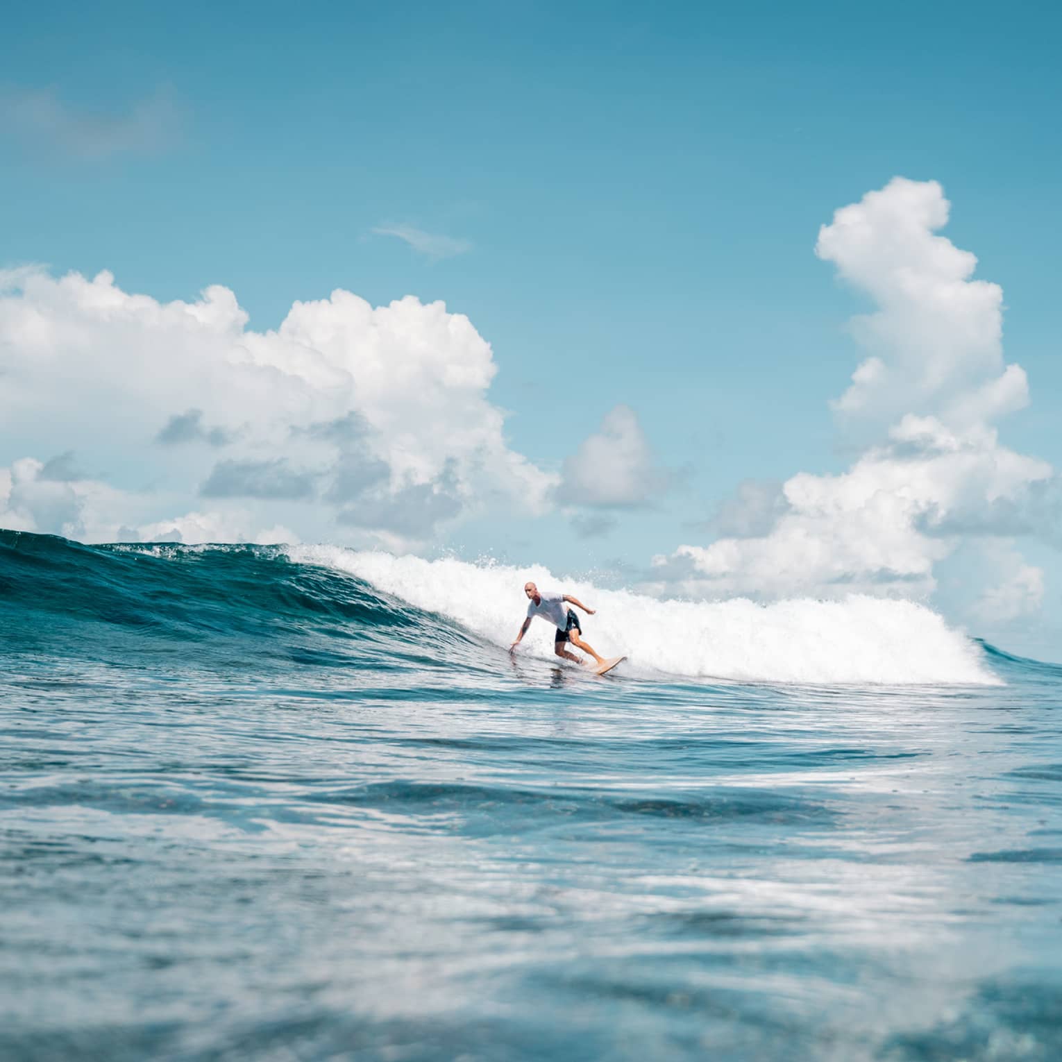 Man surfing and bending to touch wave on bright blue ocean with blue sky above