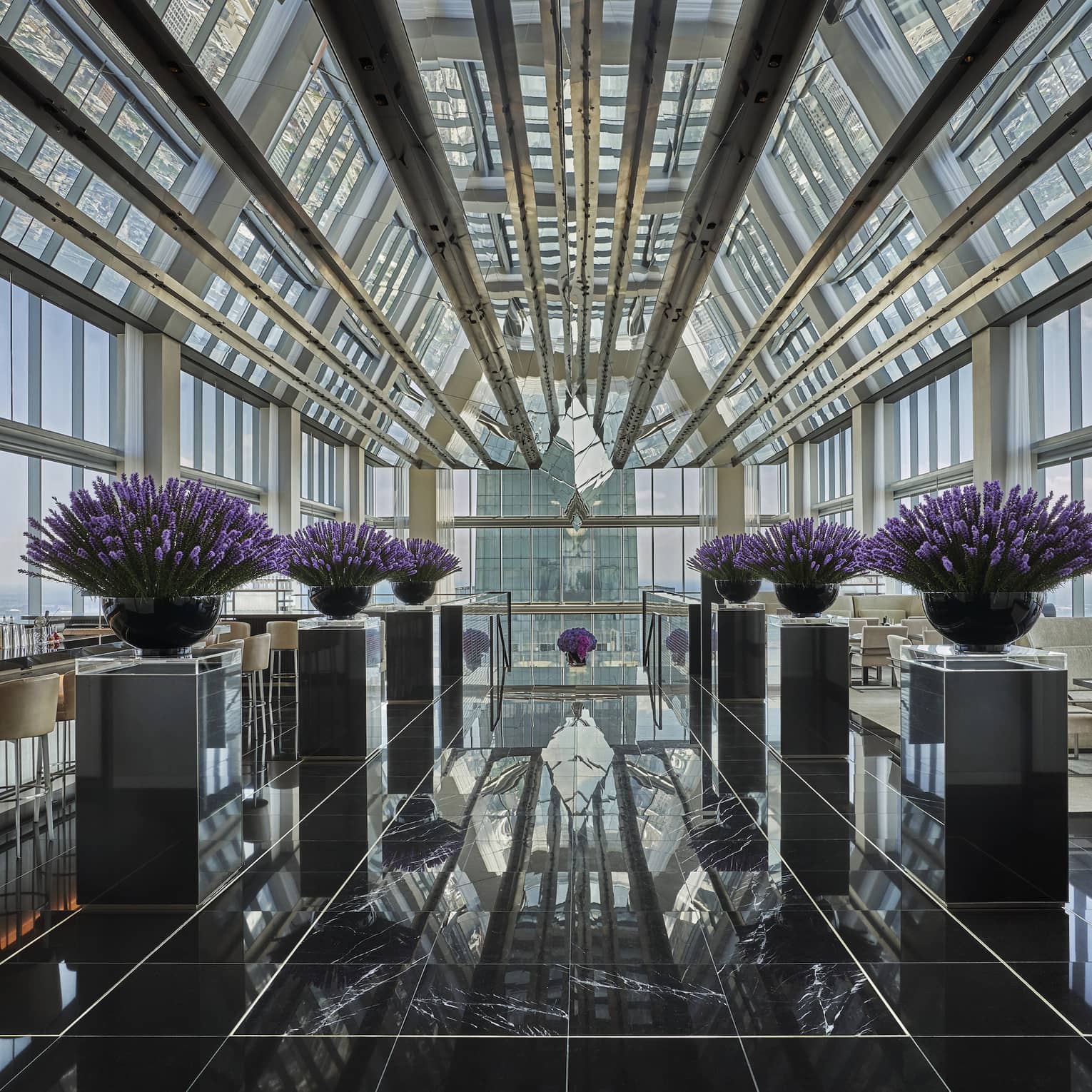 Bar beside purple flowers in black planters, marble floor under glass loft penthouse ceiling