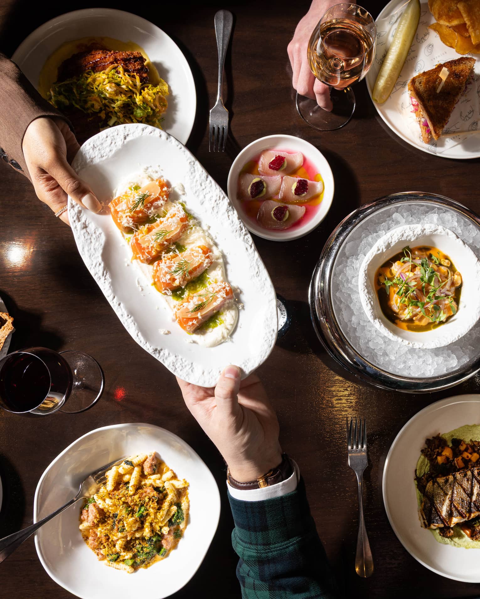 A dark wooden table topped with various colourful culinary dishes and glasses of wine