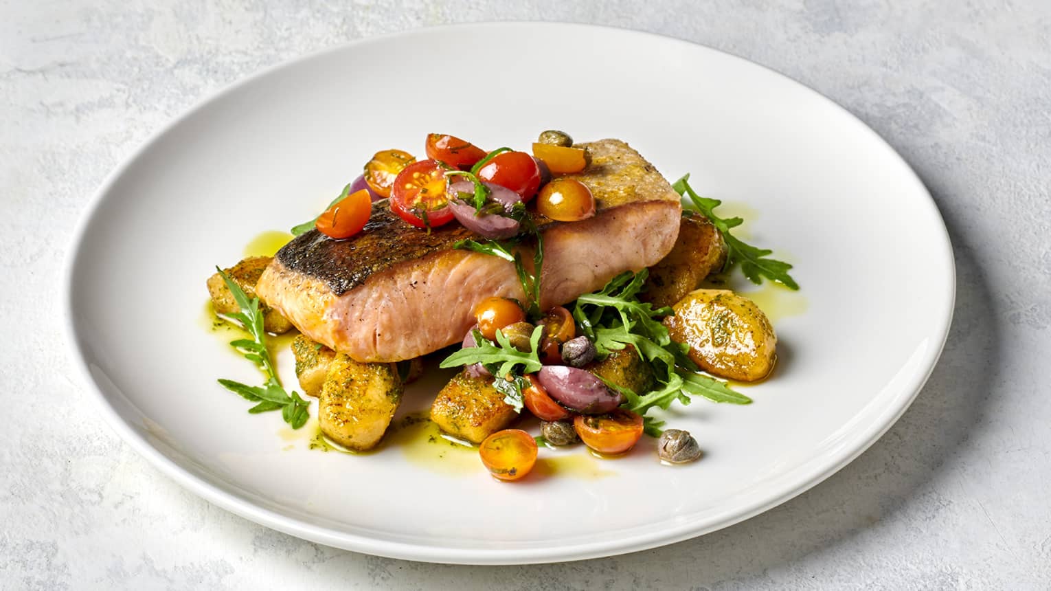 Pan-seared Salmon on white plate with Pesto Gnocchi, Wilted Rocket and Vierge Dressing