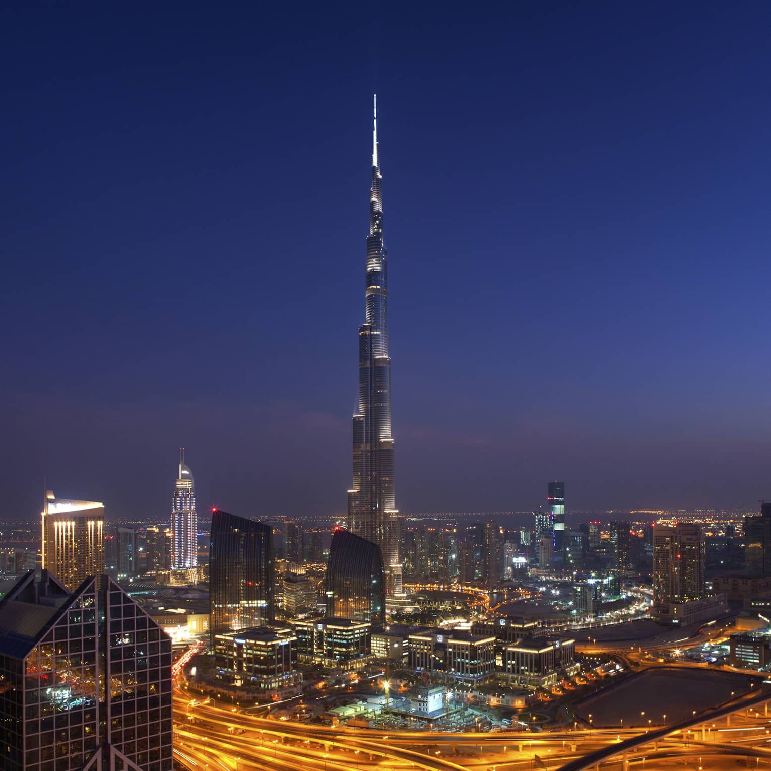 The Burj Khalifa towering over downtown Dubai under a dark starless sky, the city lit by the glow of cars and buildings.