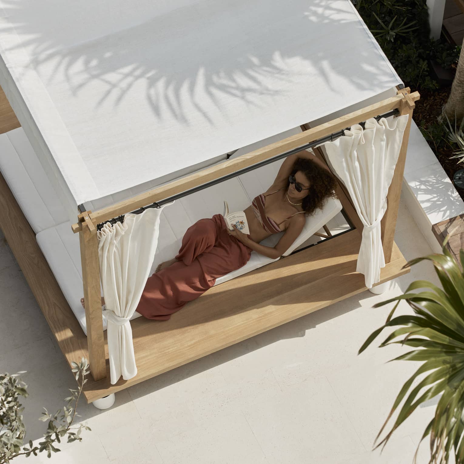Aerial view of woman lounging in a covered poolside daybed