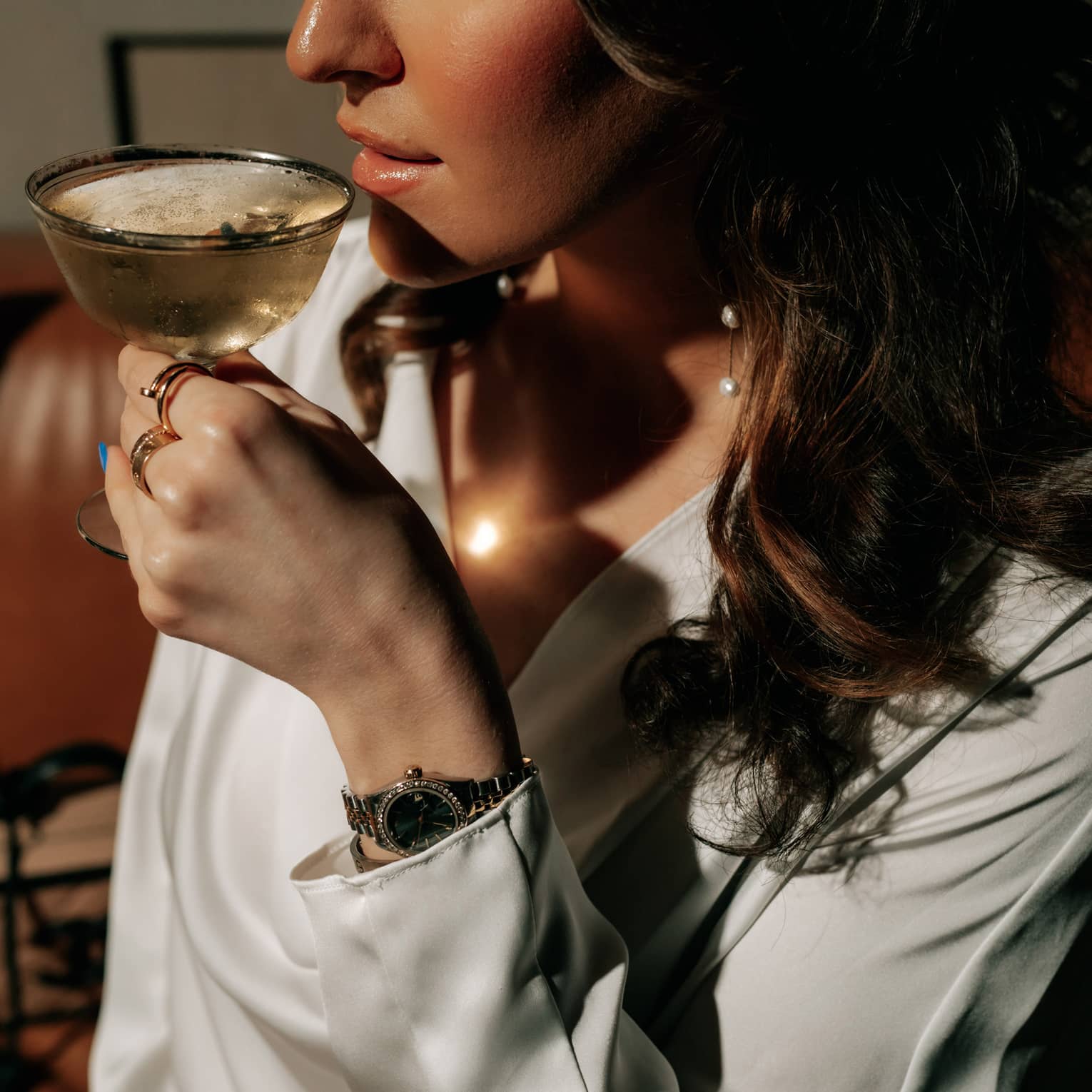 A woman with long, dark hair is about to sip a cocktail from a coupe glass.