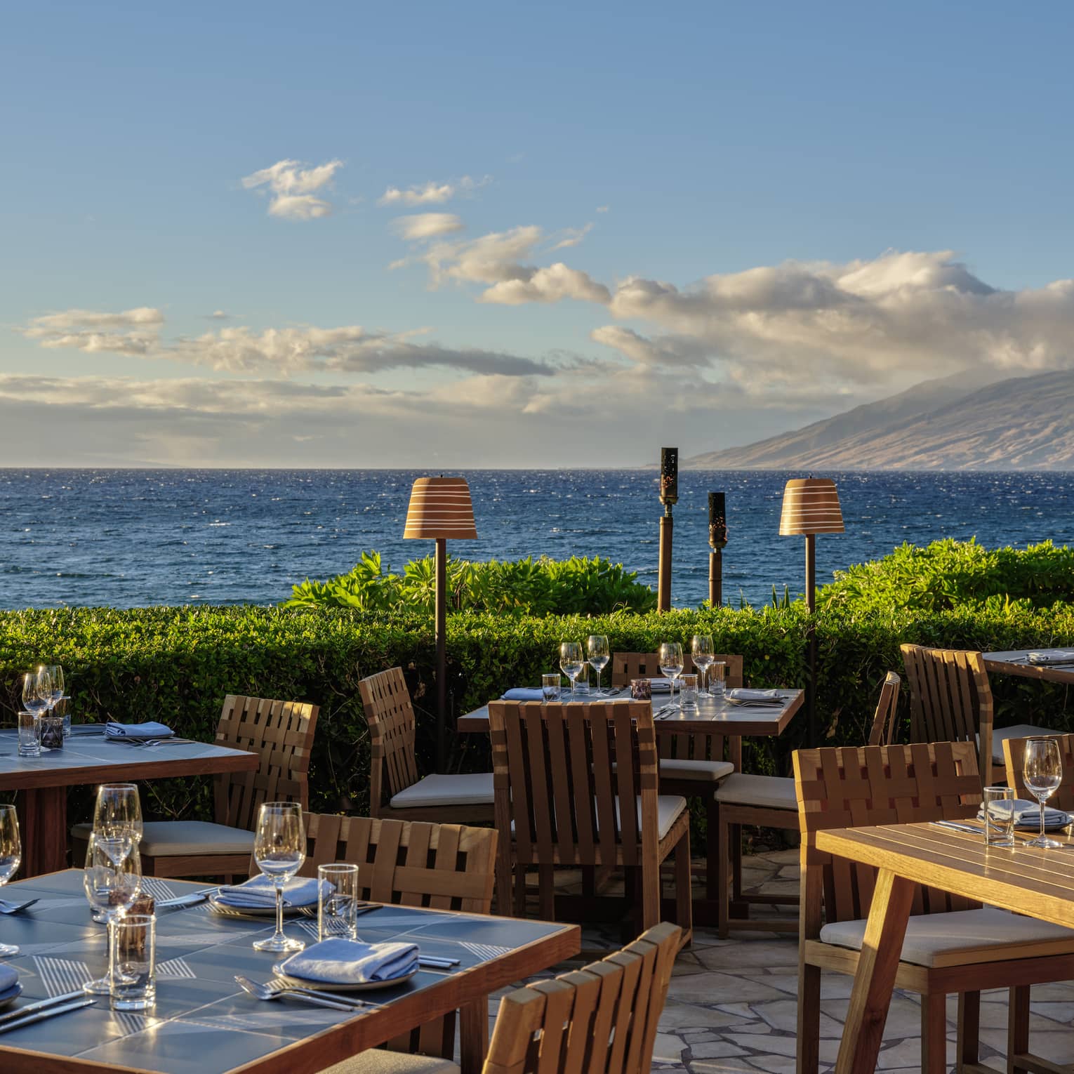 Oceanfront outdoor dining area with wooden tables and chairs set for service