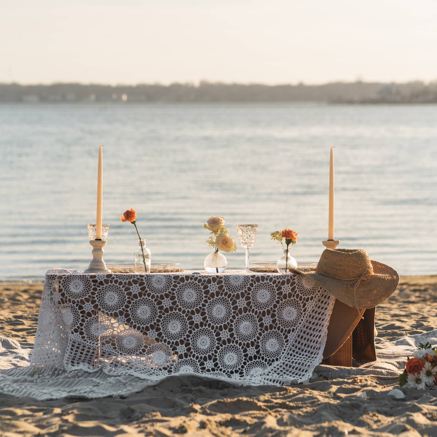 Picnic table with white tablecloth set up on private beach at sunset