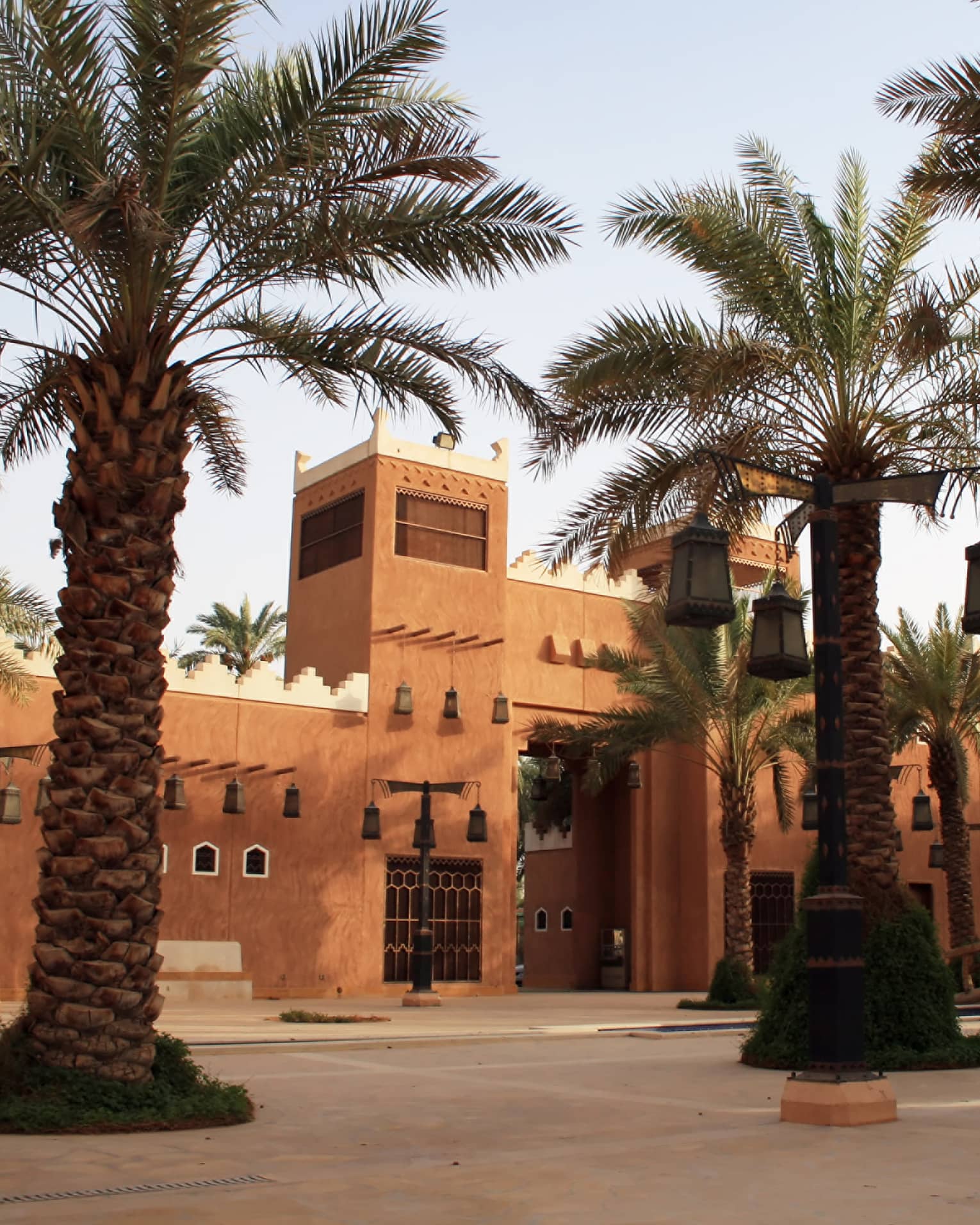 Sunny exterior of sandstone building and large palm trees with lanterns hanging from branches