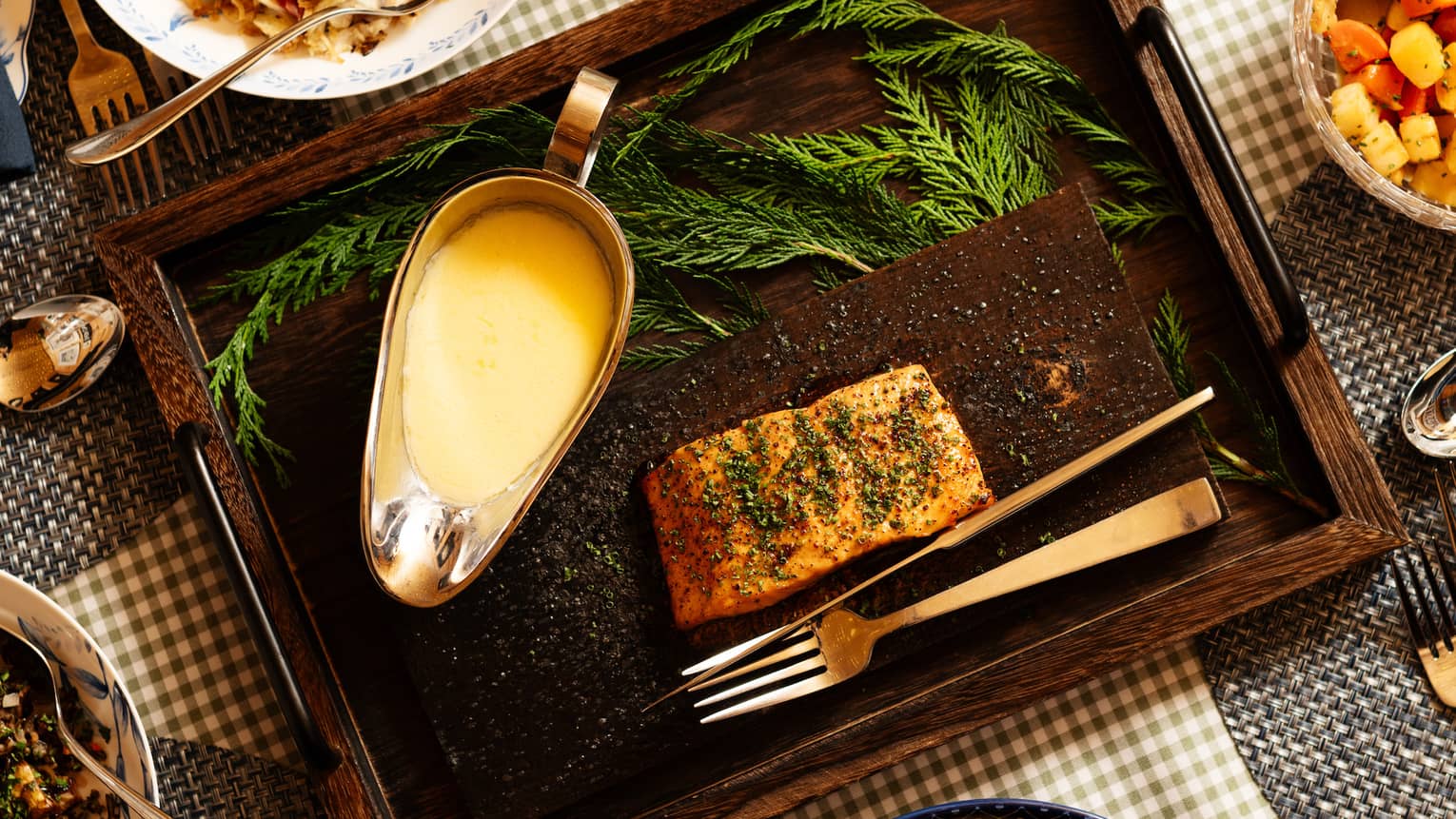 A salmon dish with a creamy sauce served on a plank in a wooden tray, surrounded by various other colourful vegetable-based dishes