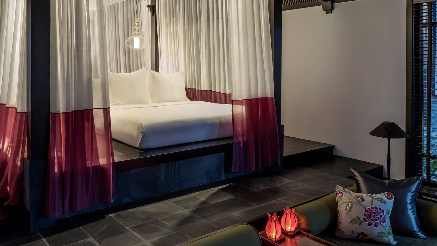 One-bedroom villa raised platform bed under sheer white-and-red drapes