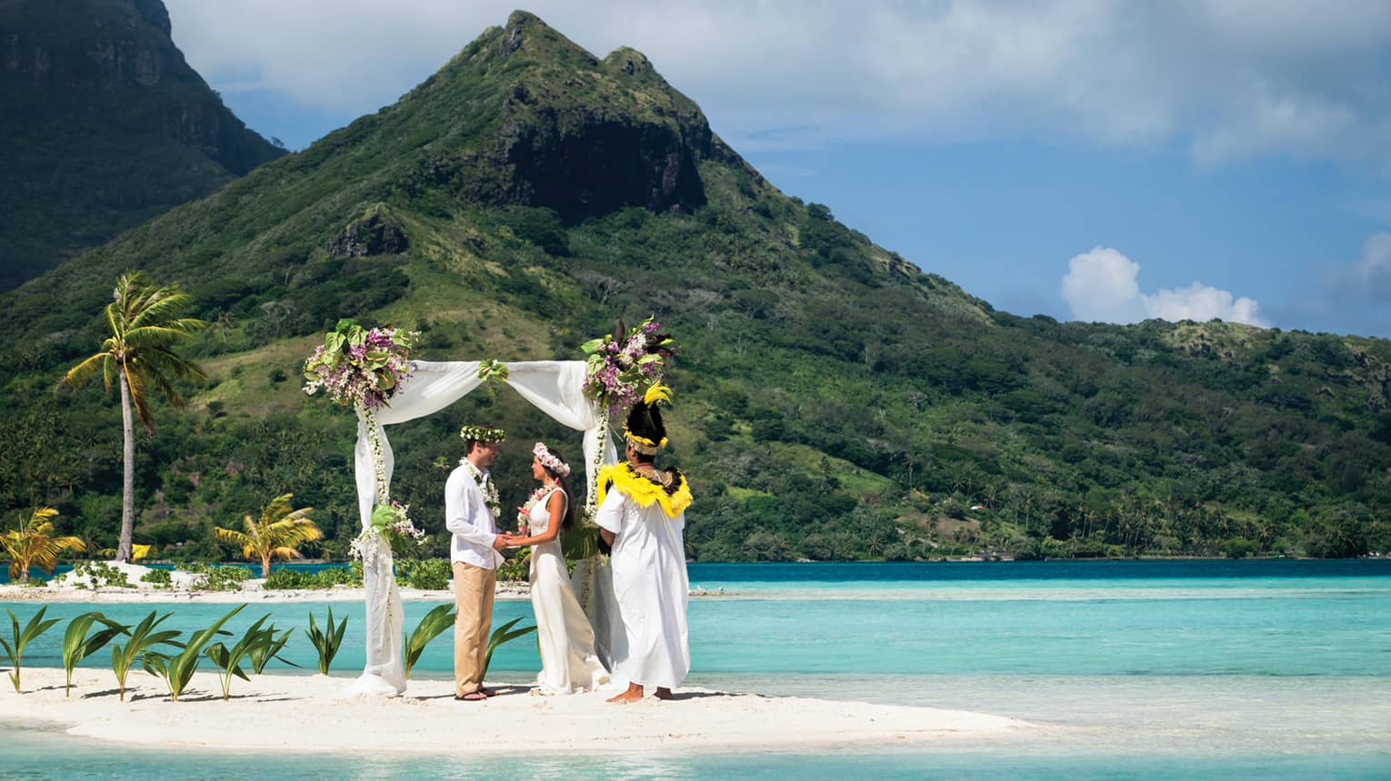 Wedding ceremony under altar draped in sheer white fabric on white sandbar by mountain