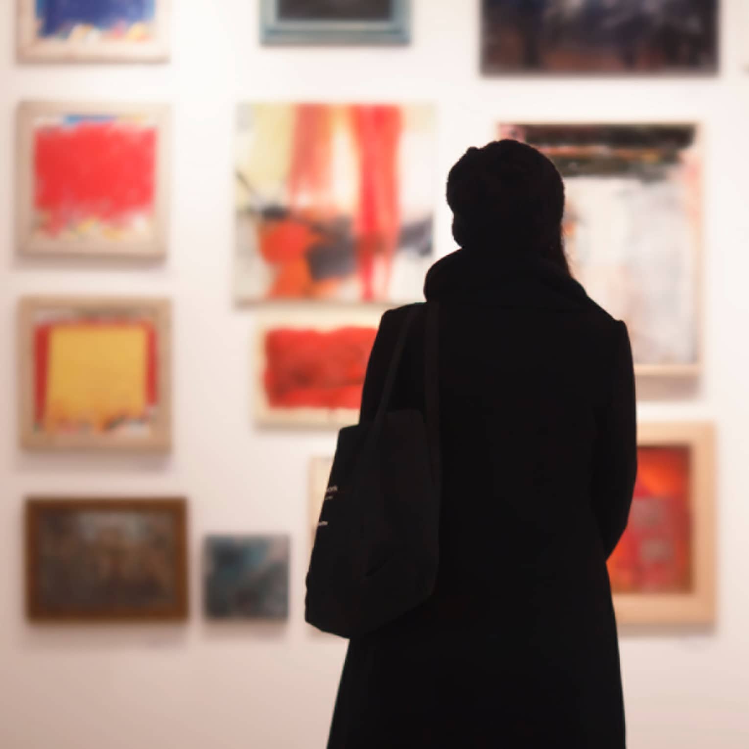 Silhouette of back of woman with hat bag looking at gallery wall with colourful art