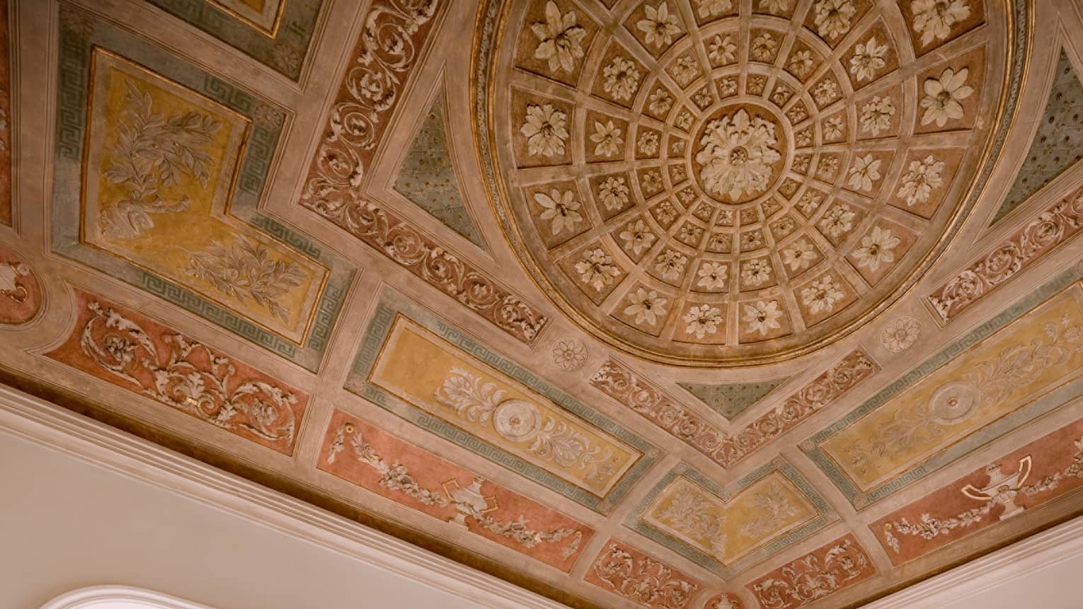 Fresco suite with elegant decor, featuring a king-sized bed, a seating area with beige furniture, a large window with city views, and a ceiling adorned with intricate frescoes.