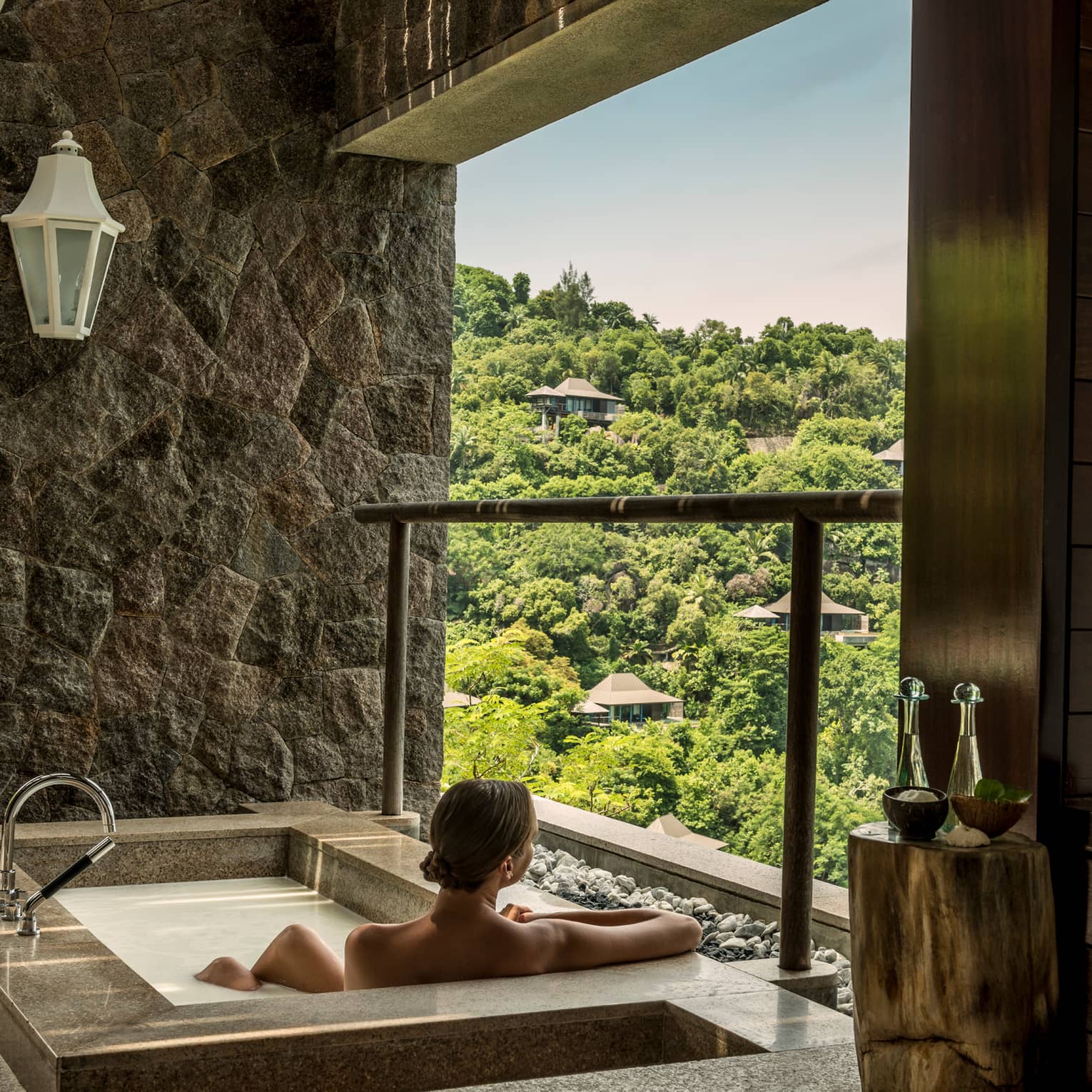 Back of woman sitting in rectangular hot tub, looking out open wall at mountain
