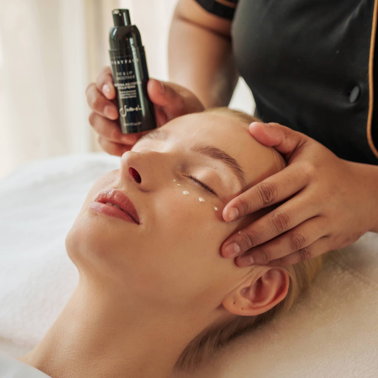 Guest lies with eyes closed as a spa attendant places product under their eyes