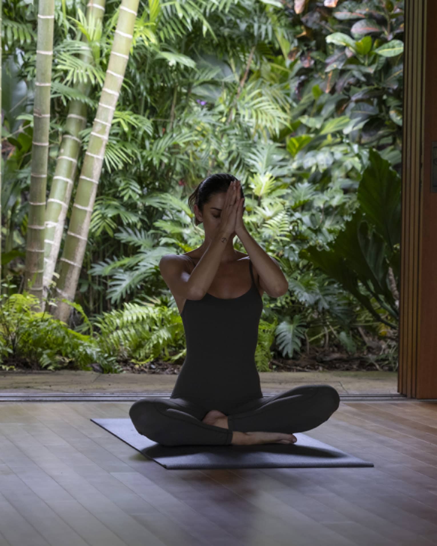 A woman sits cross-legged, practising yoga in spa hale at tropical luxury resort