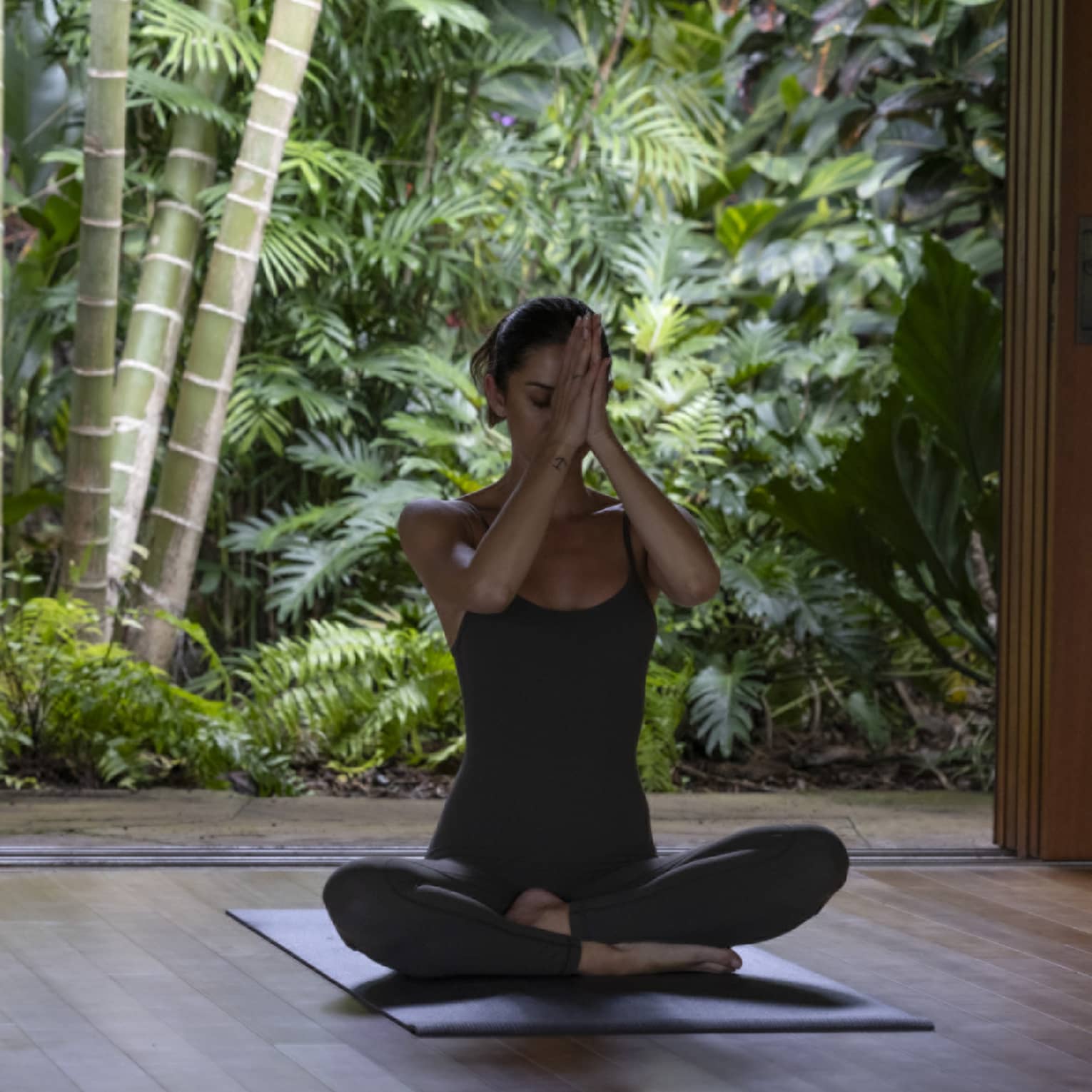 A woman sits cross-legged, practising yoga in spa hale at tropical luxury resort