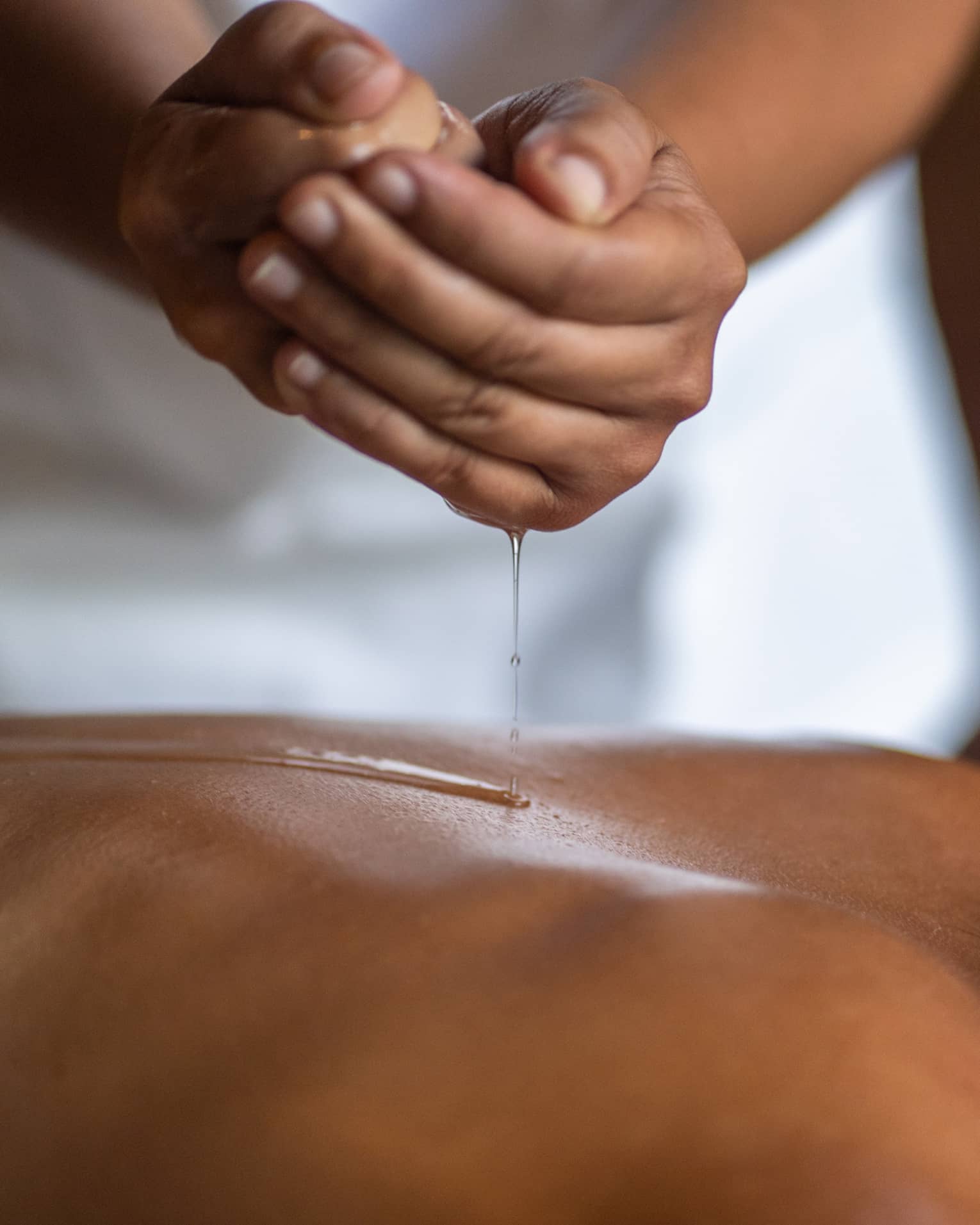Delicate hands apply oil to a guest's back during a spa treatment