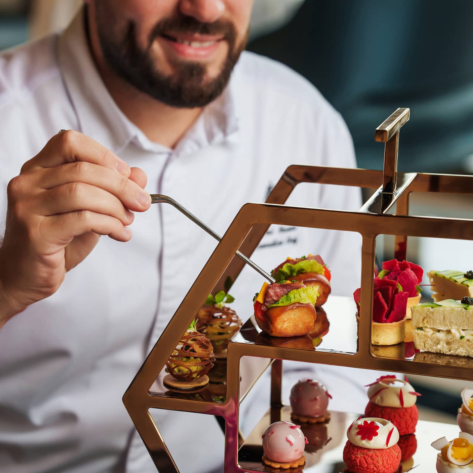 Close up of man with wearing a white button-down shirt organizing pastries on a three-tiered tray for afternoon tea