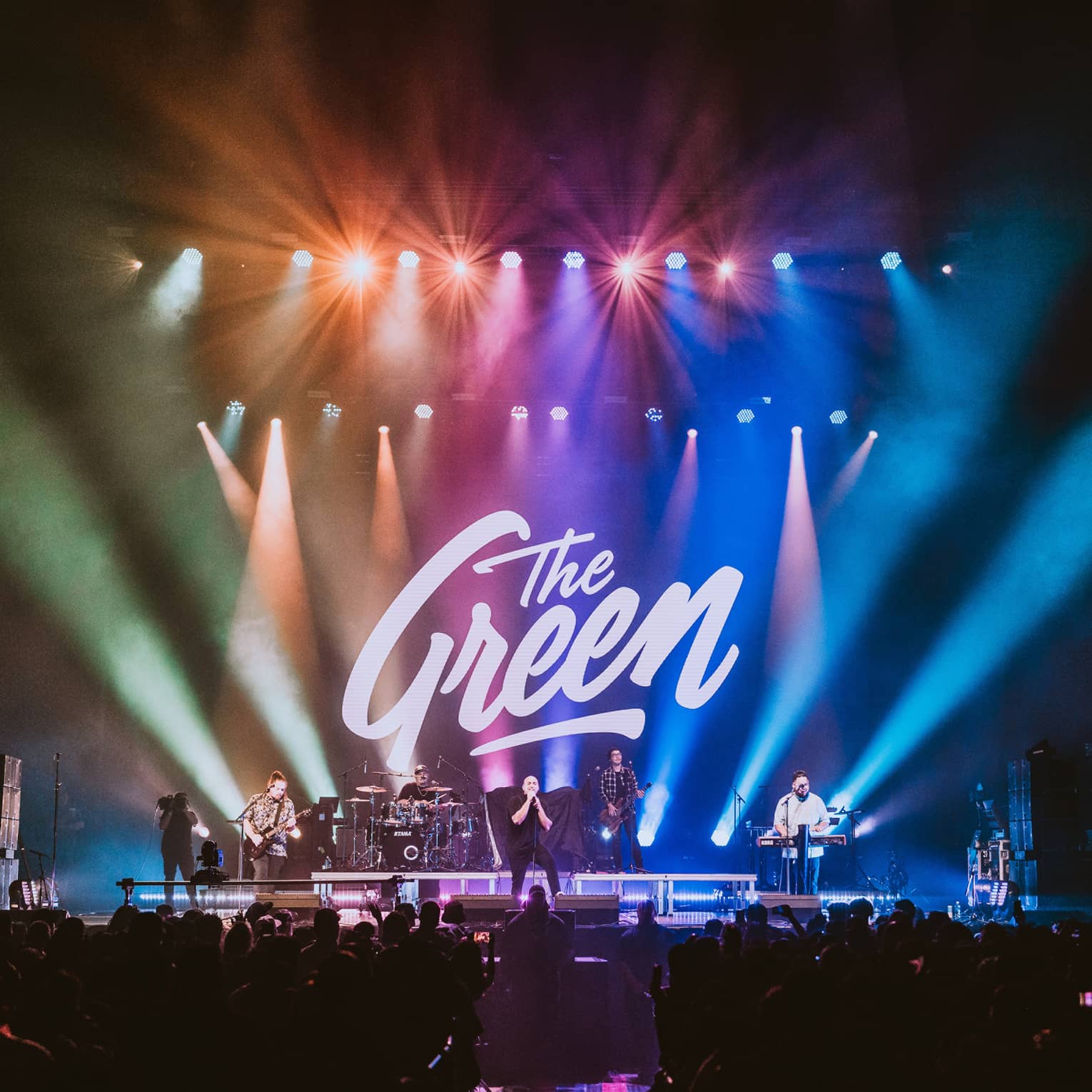 Musicians perform on stage illuminated with rainbow-lit backdrop featuring The Green signage