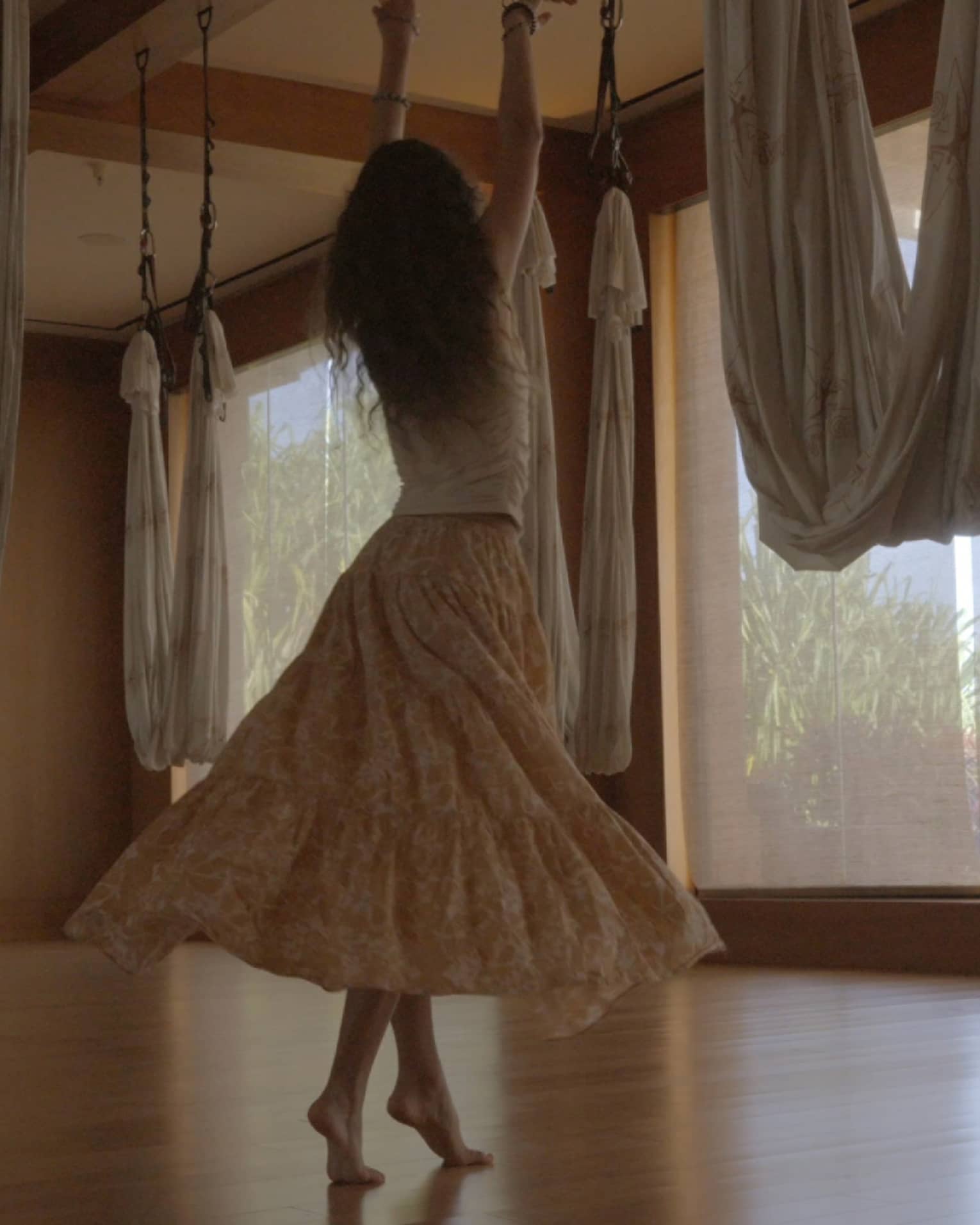 A woman dances in movement studio featuring hanging aerial yoga hammocks
