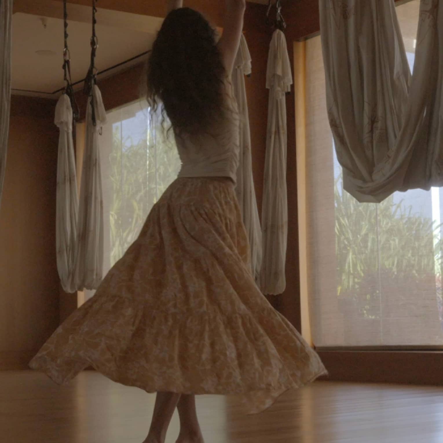 A woman dances in movement studio featuring hanging aerial yoga hammocks