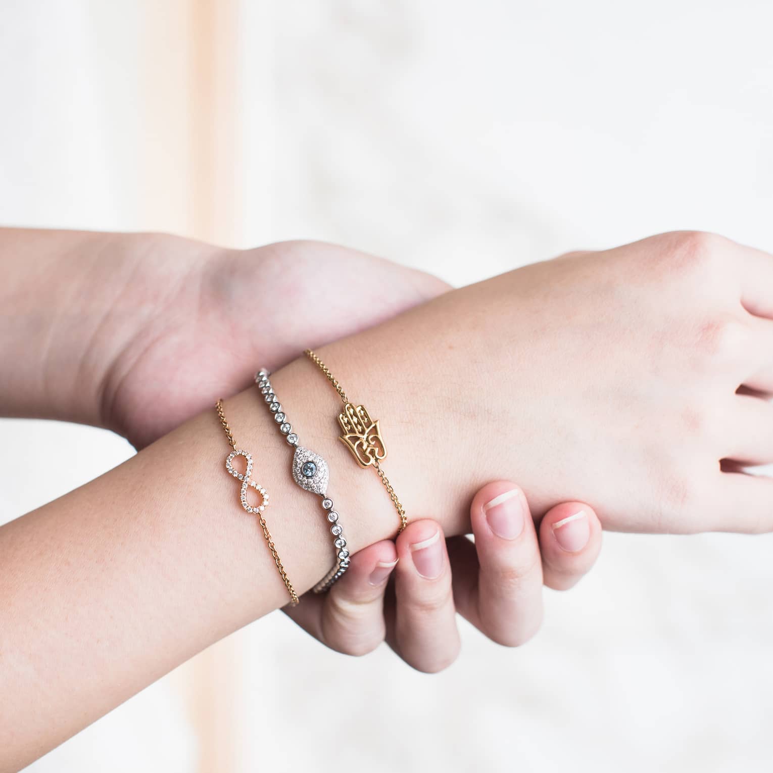 Three delicate bracelets adorn a person's wrist that is being held by another hand