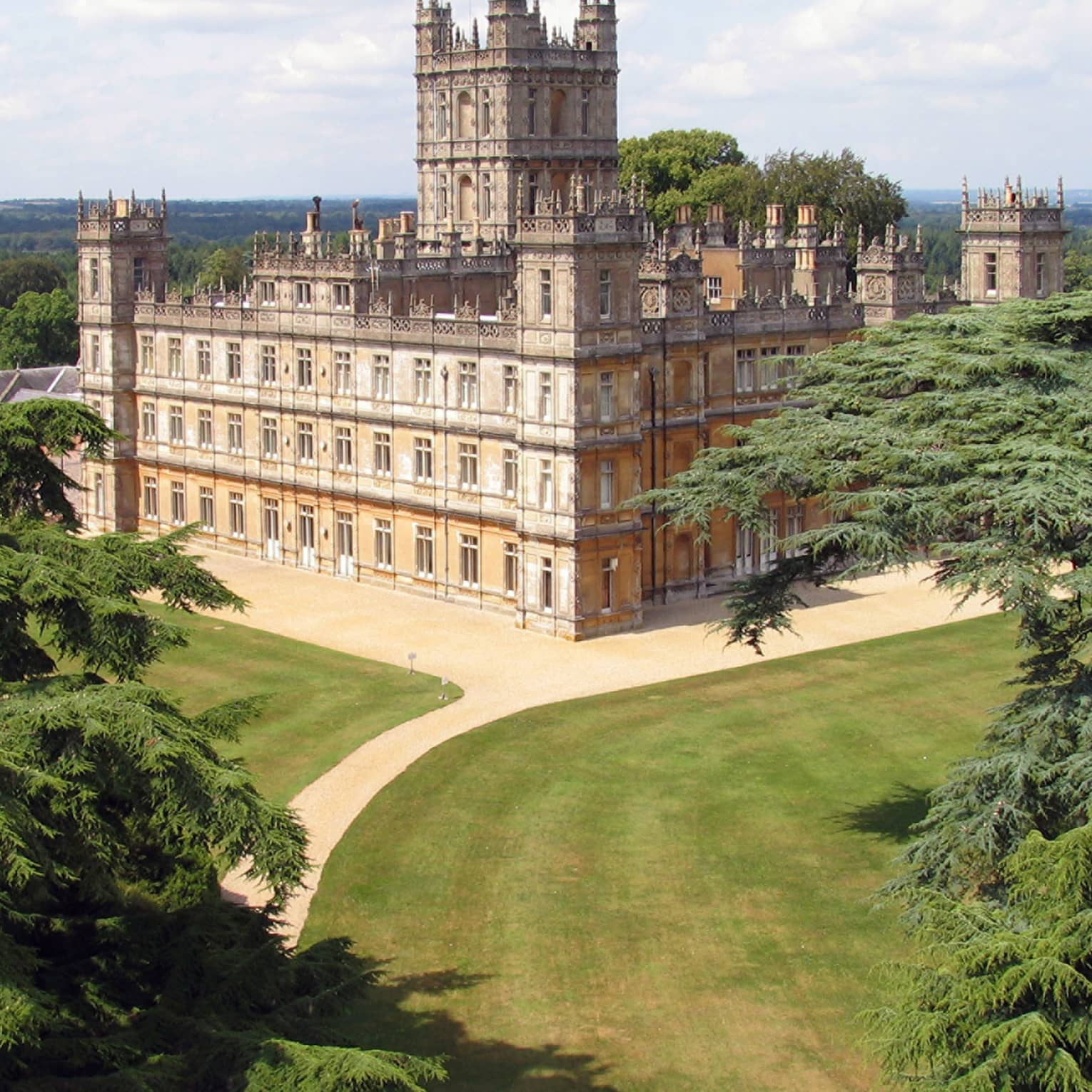 View over rolling green hills, trees to large Highclere castle building