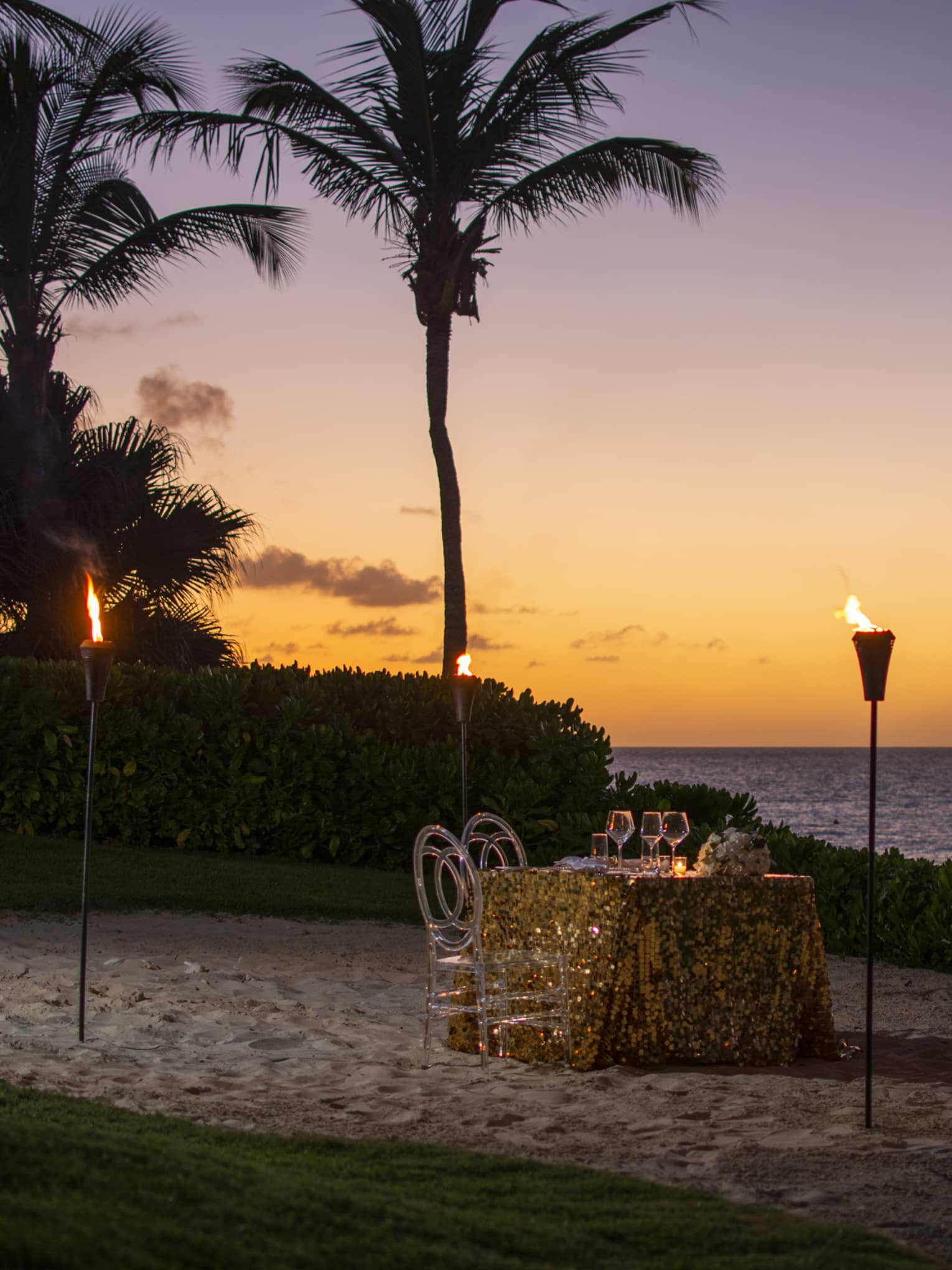 Romantic beachfront dinner setup with tiki torches and a sunset ocean view.