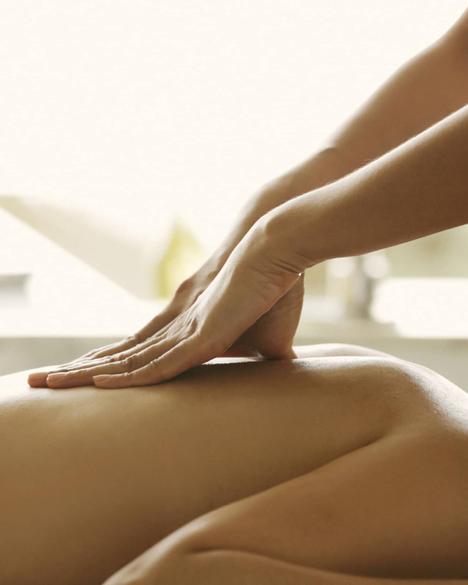 Masseuse reaches over, massages woman's bare back as she lies on spa table