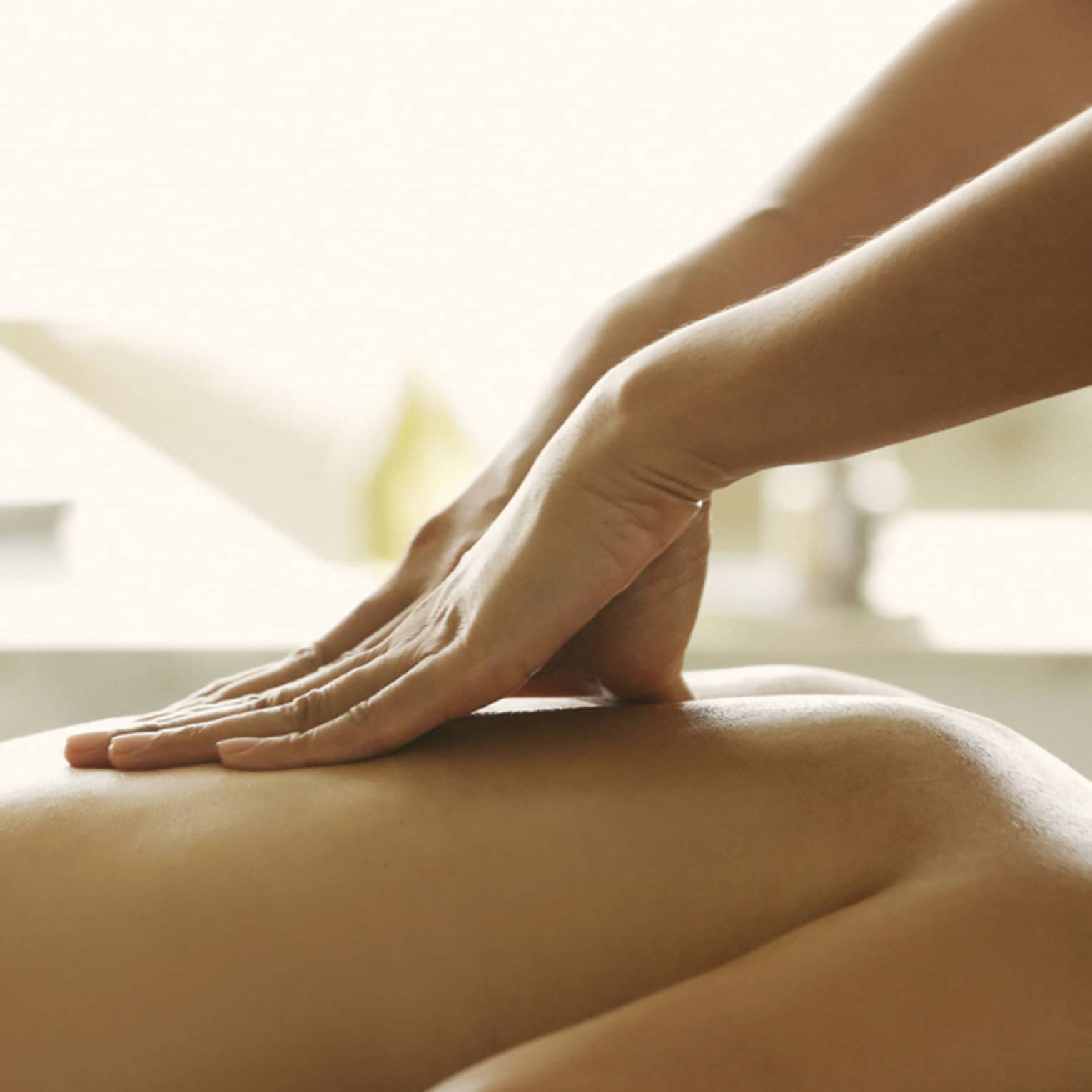 Masseuse reaches over, massages woman's bare back as she lies on spa table