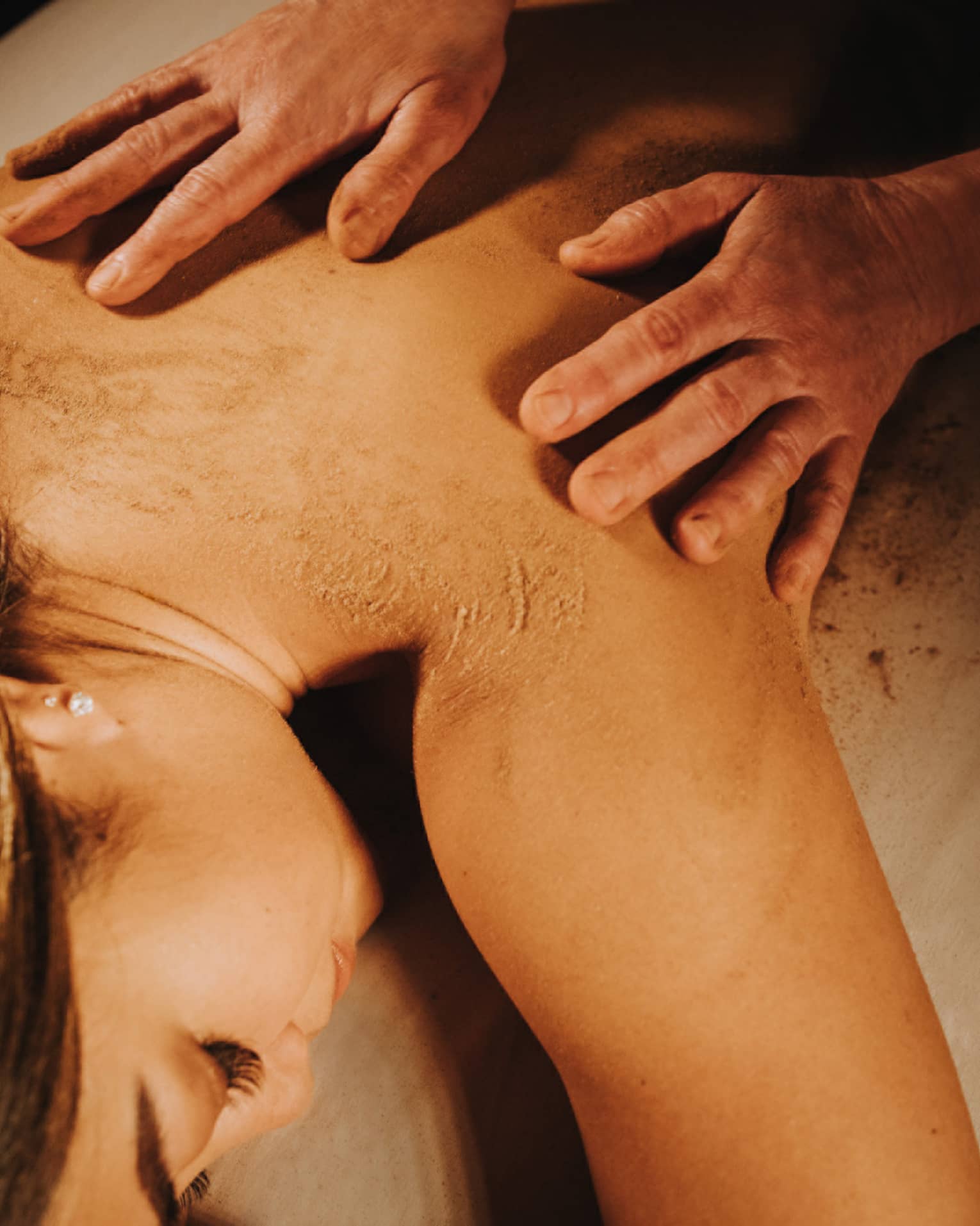Two hands on woman's bare back as she lays on massage table in dimly lit room