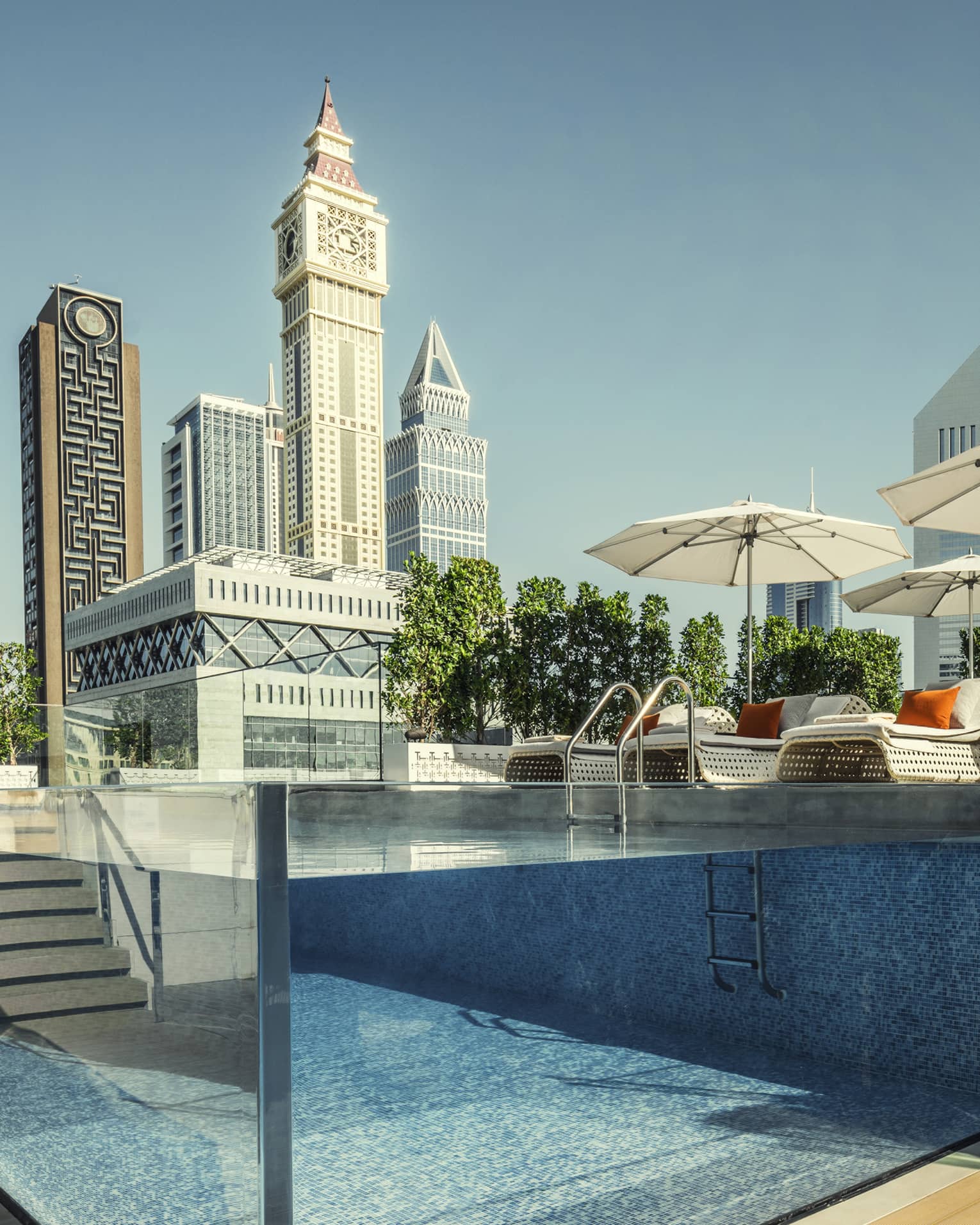 Raised glass plunge pool by stairs on patio deck, lounge chairs, umbrella