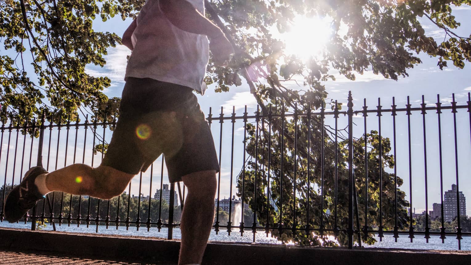 Close-up of lower half of man jogging by wrought-iron gates on New York City waterfront path