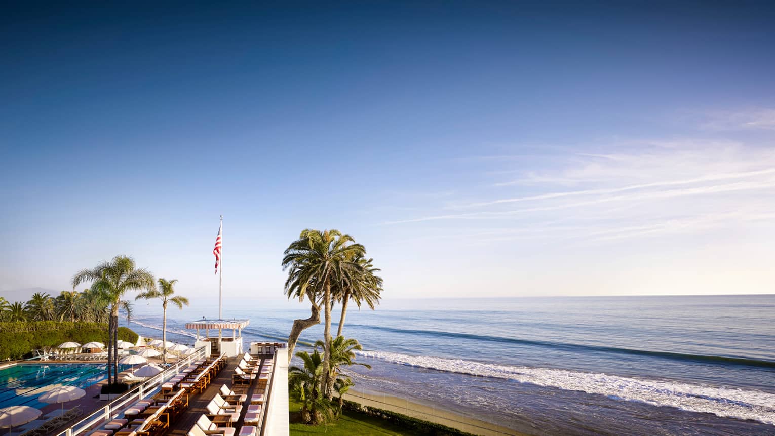 Blue sky over beach, palm trees by hotel outdoor swimming pool and lounge chairs 