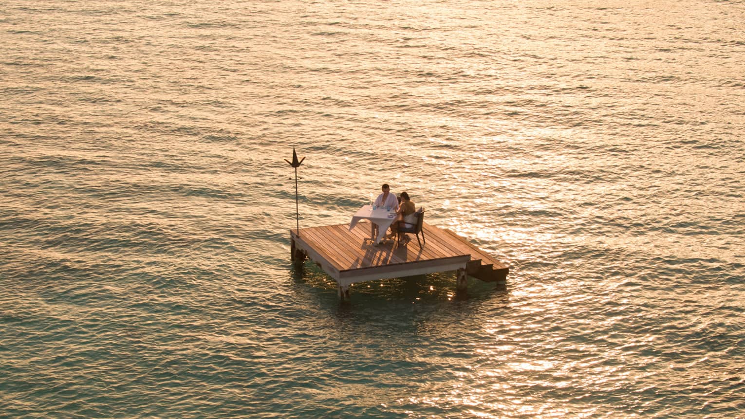 Aerial view of couple dining on small floating wood platform on moonlit lagoon
