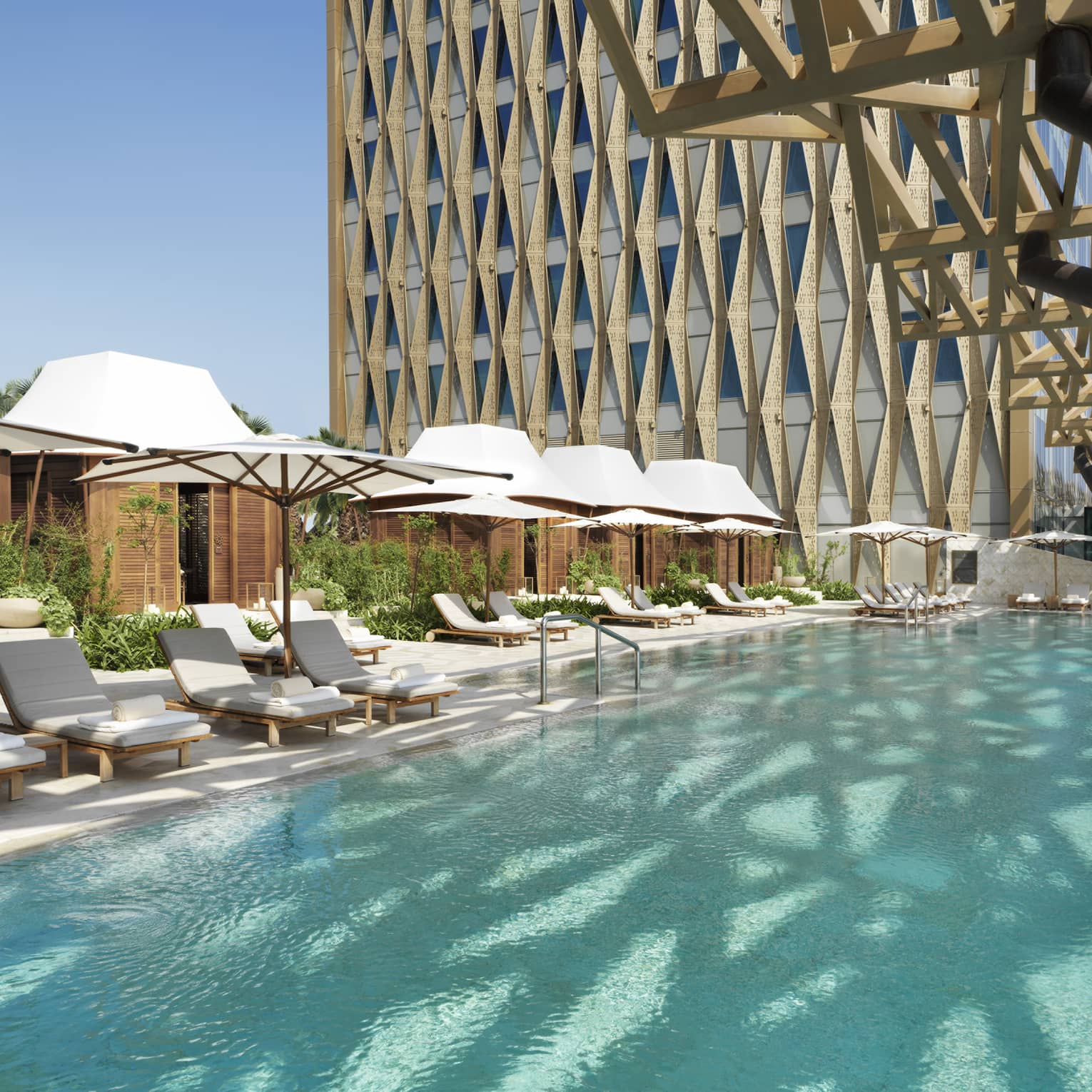 An olympic size pool surrounded by lounge chairs shaded by large white umbrellas