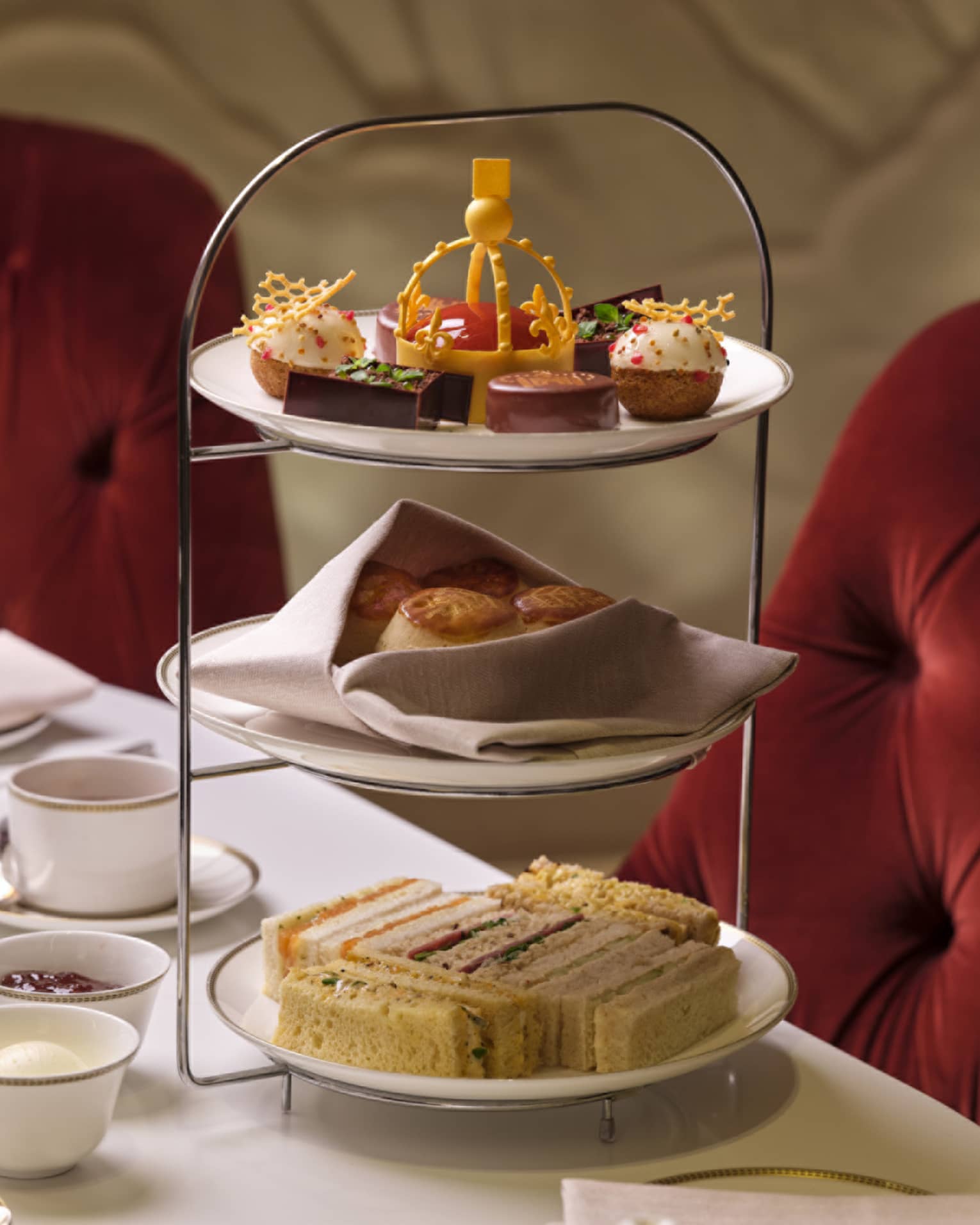 Tea stand with finger sandwiches, treats and small bites on table beside tea and champagne