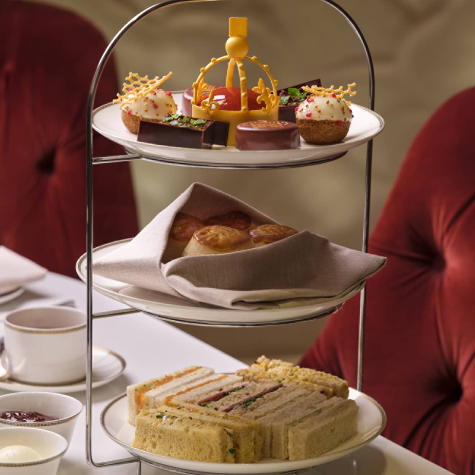 Tea stand with finger sandwiches, treats and small bites on table beside tea and champagne