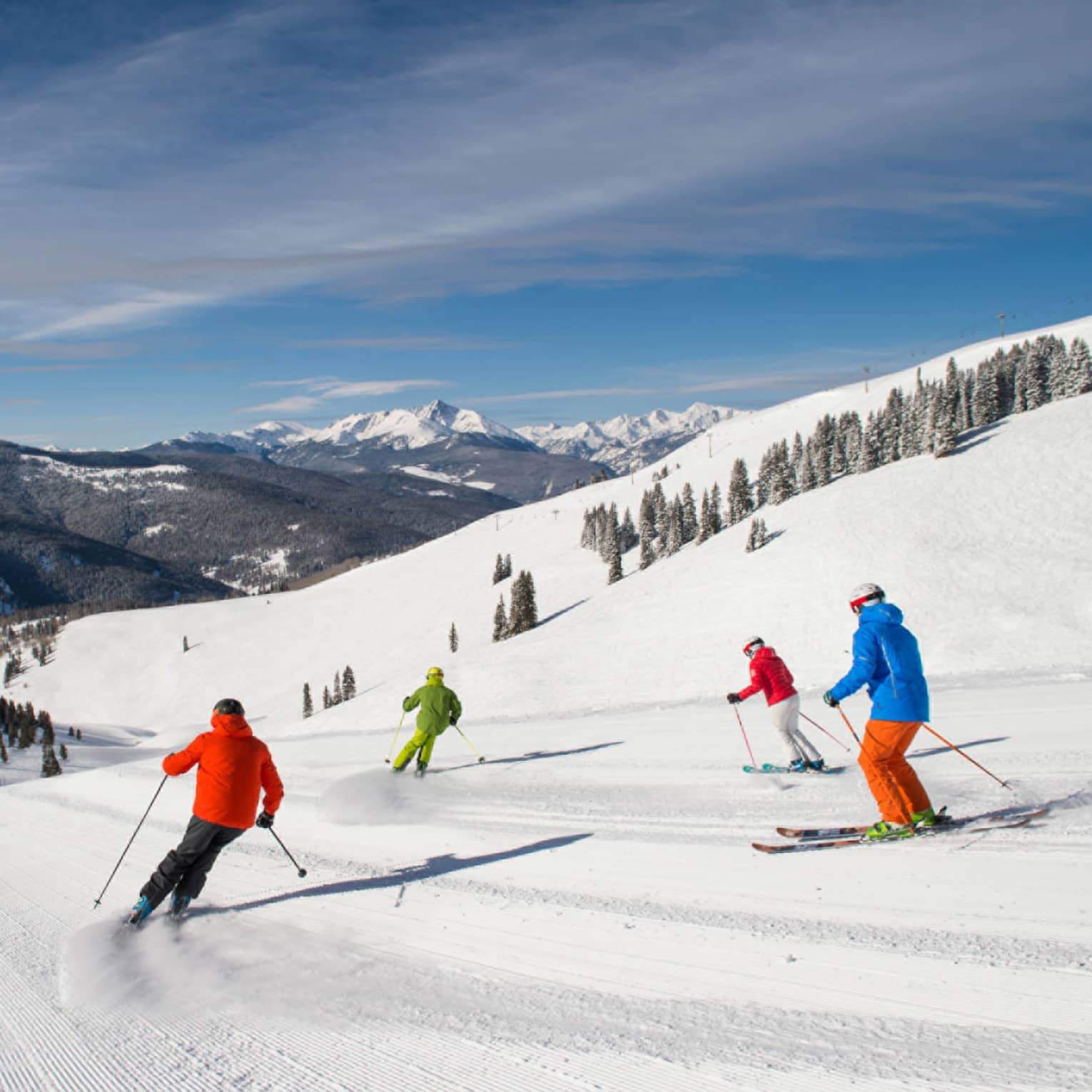 Four skiers in brightly coloured coats ski down mountain covered in snow
