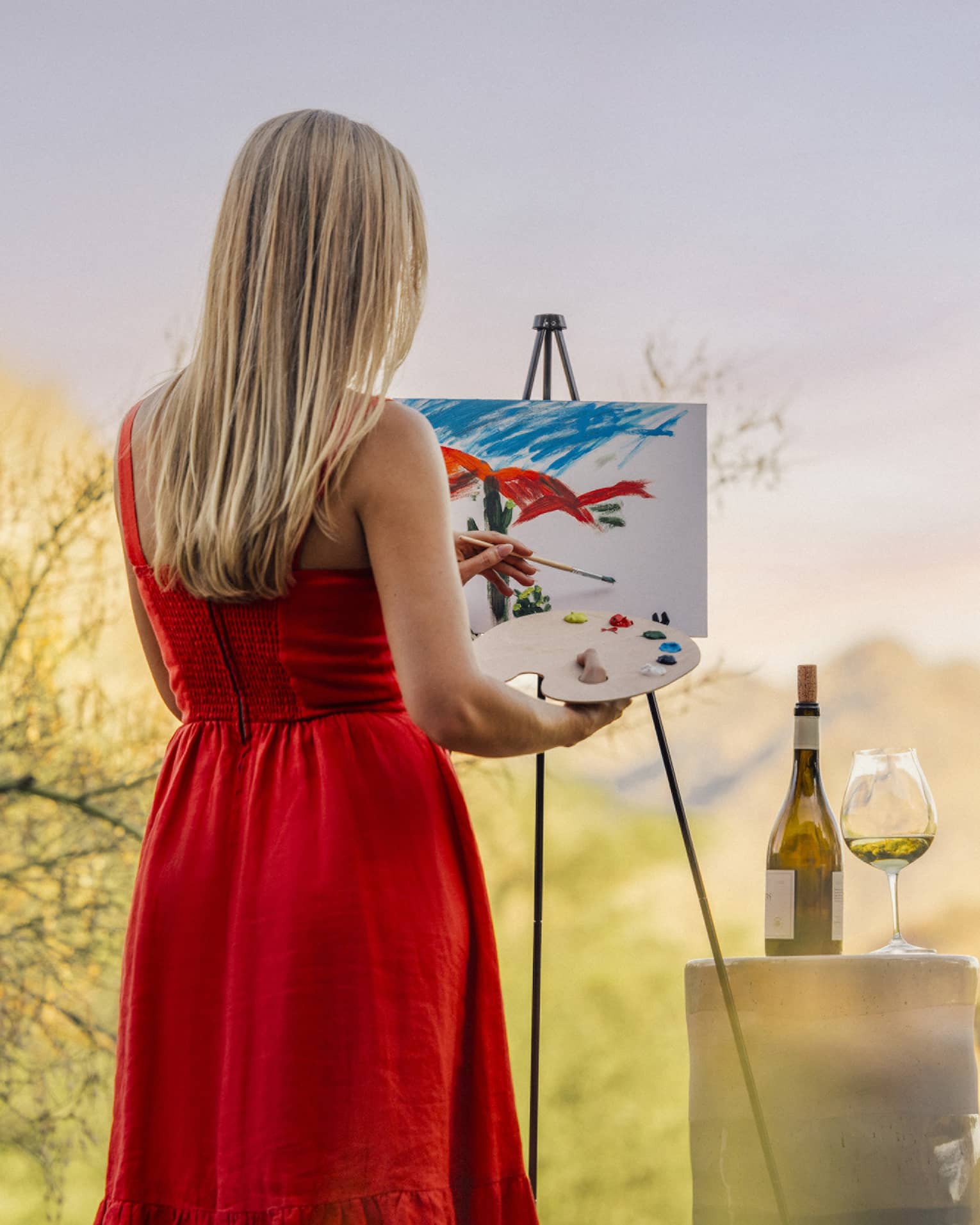 Person wearing a red dress and painting with a wine glass beside them.
