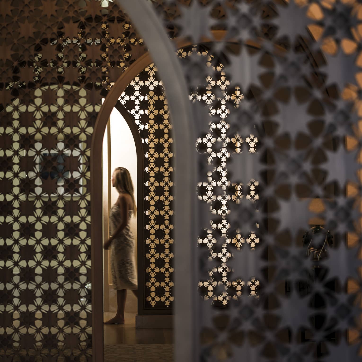 Woman in white wrap walks through dimly-lit decorative entranceway in hall