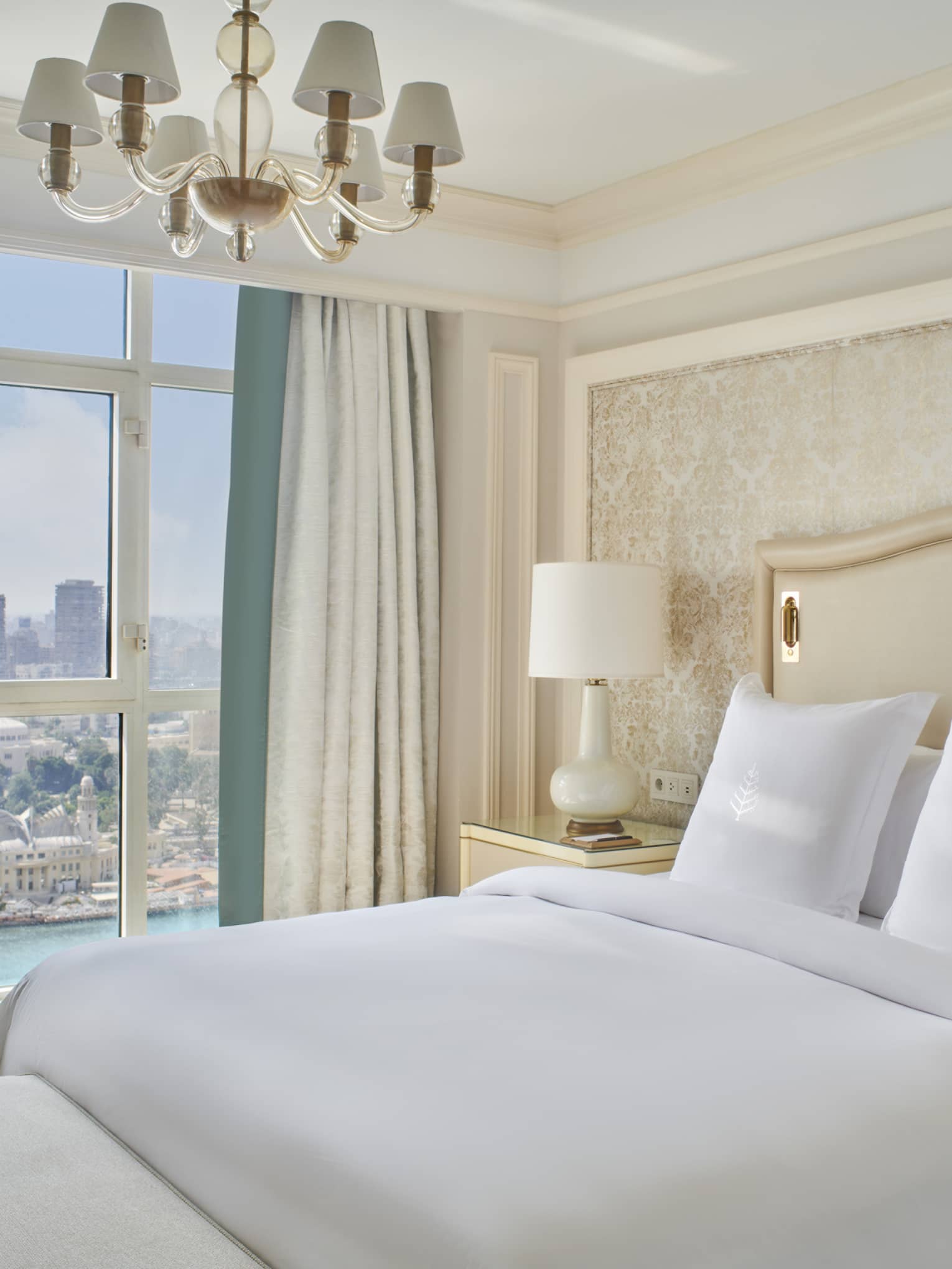 Guest bedroom with king bed, white linens and cream tufted headboard; floor-to-ceiling window with views of the River Nile