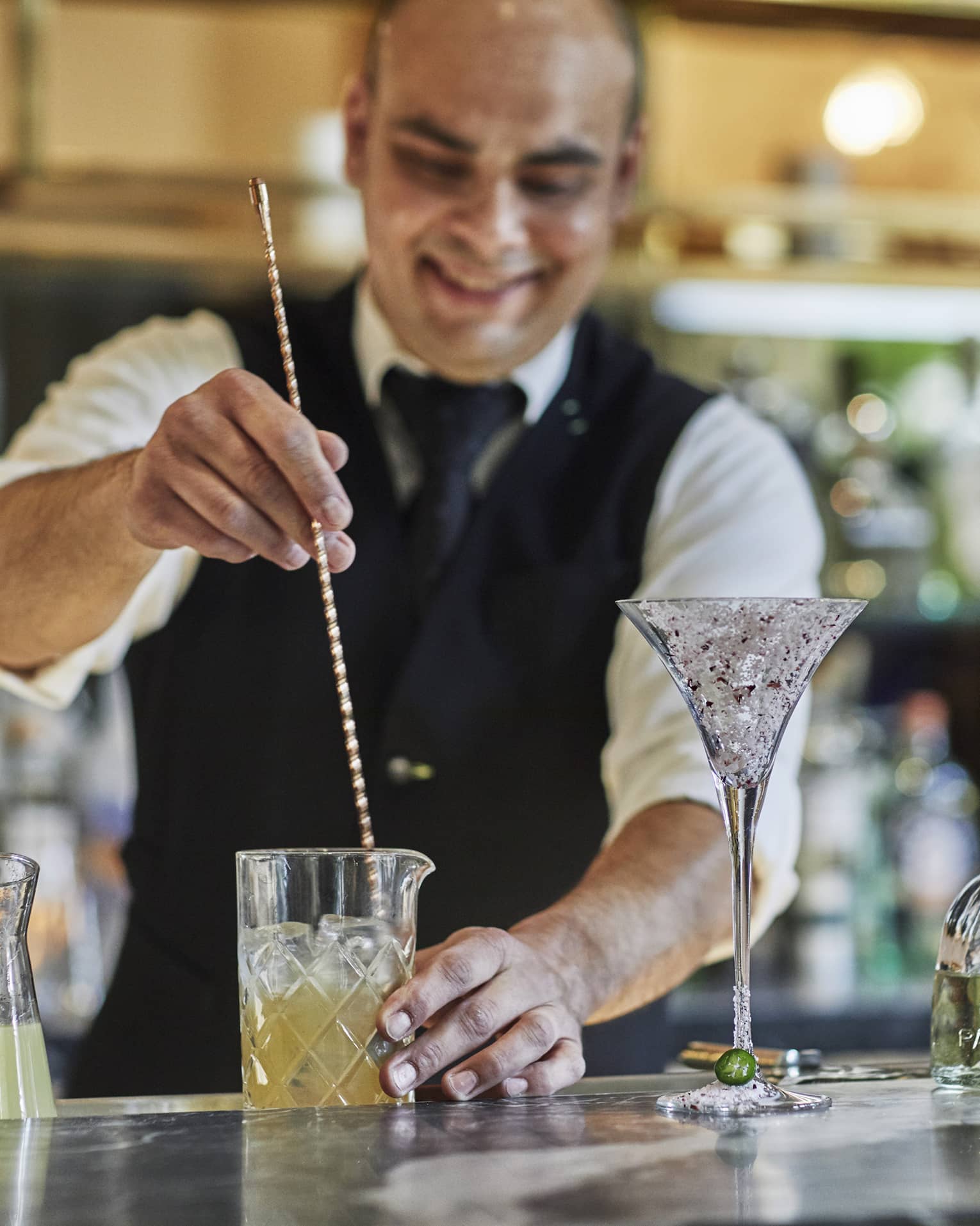 Bartender stirs cocktail with large swizzle stick on bar 
