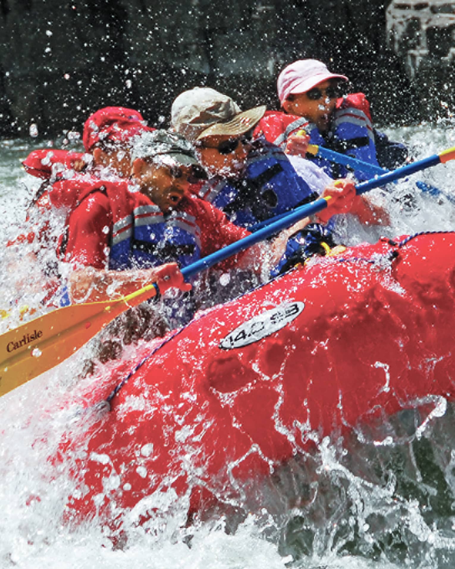 Water sprays around red inflatable raft, people with paddles, life vests white water rafting