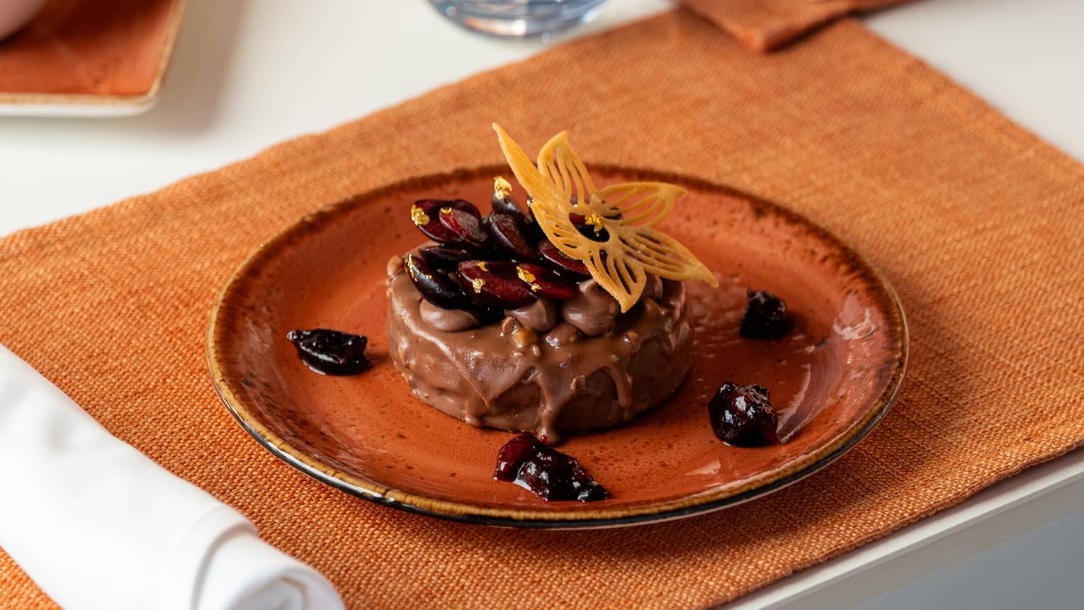 Pecan praline chocolate cake topped with an orange edible flower served on an orange stoneware plate