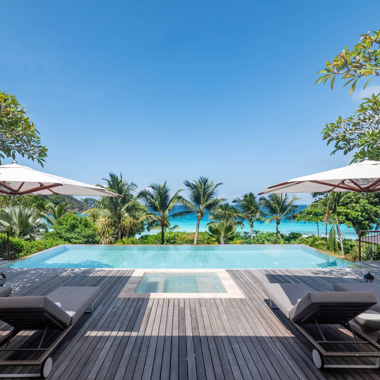 Private pool deck with lounge chairs and umbrellas, facing a pool and the turquoise sea