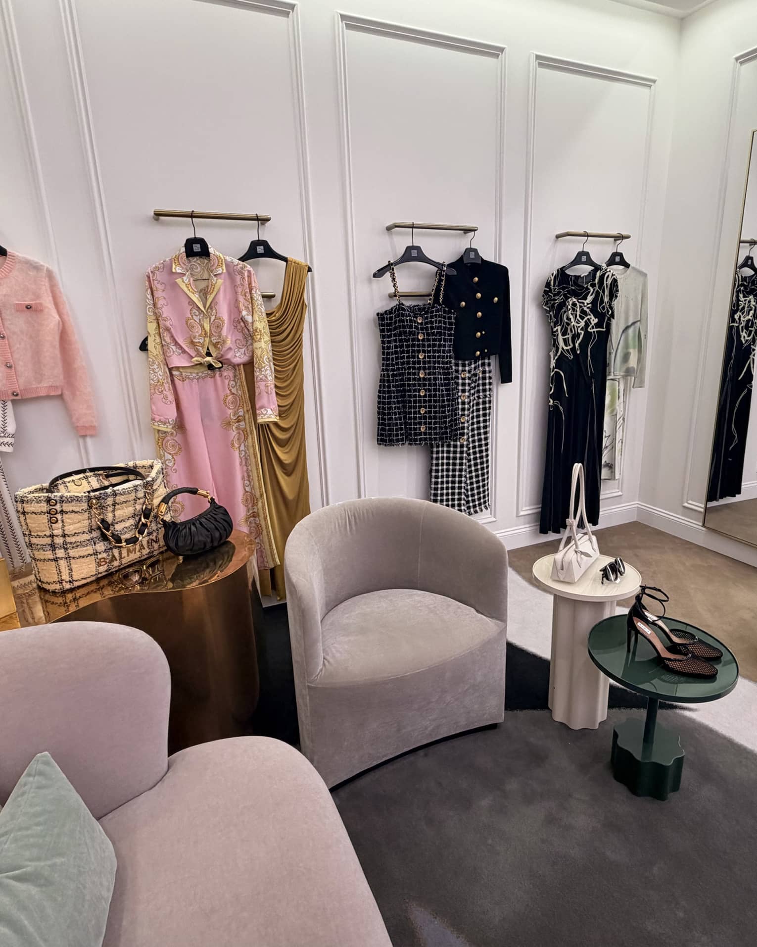 Large dressing room with arm chairs and tables and various curated outfts hung on the wall