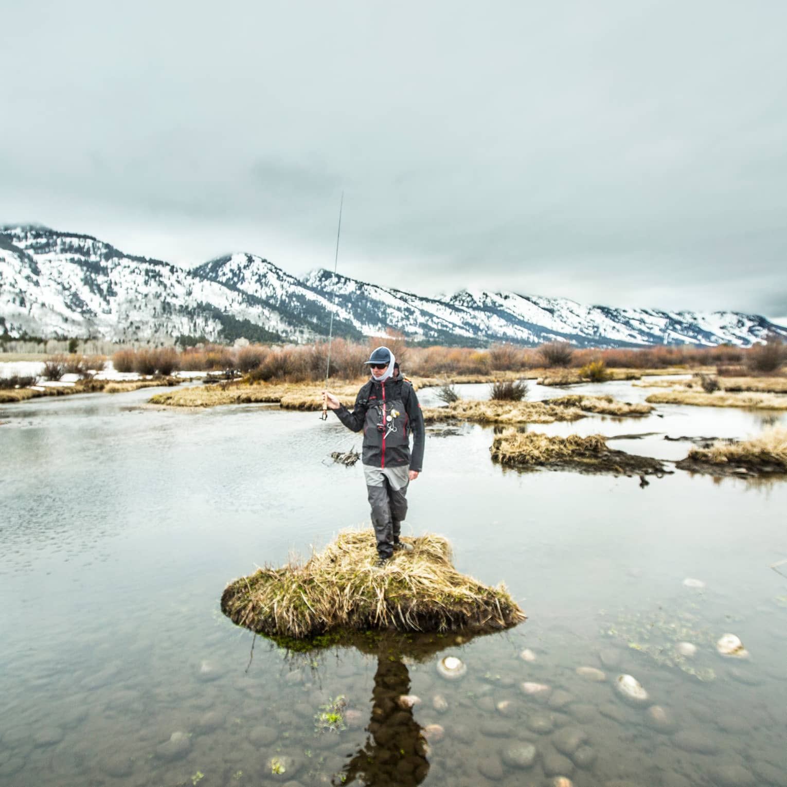 A man standing on a small piece of land surrounded by water holding a fishing rod.