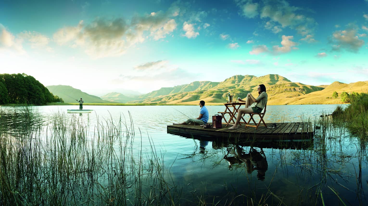 Marsh with people on wood platforms holding fishing poles and relaxing, Drakensberg Mountains in background
