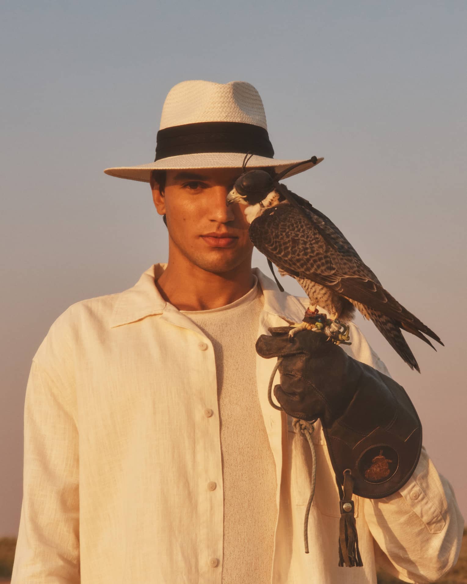 Person in straw hat and white shirt with gloved hand outstretched and hawk perched on it